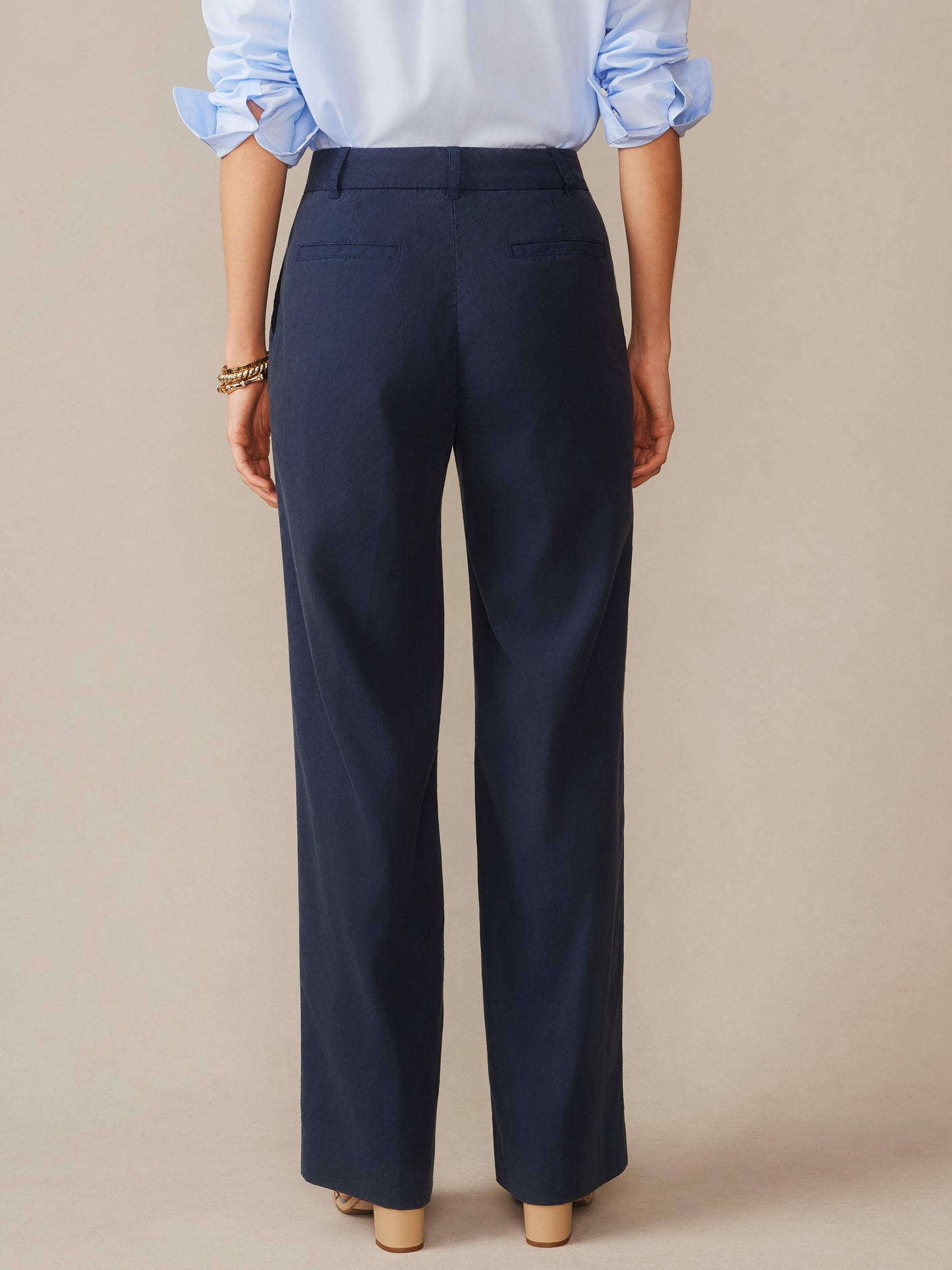 A woman wearing navy Fiona Linen Blend Pants by J.McLaughlin, paired with a light blue shirt, showcasing effortlessly stylish, enduring designs and innovative fabrics that embody a legacy of timeless fashion.