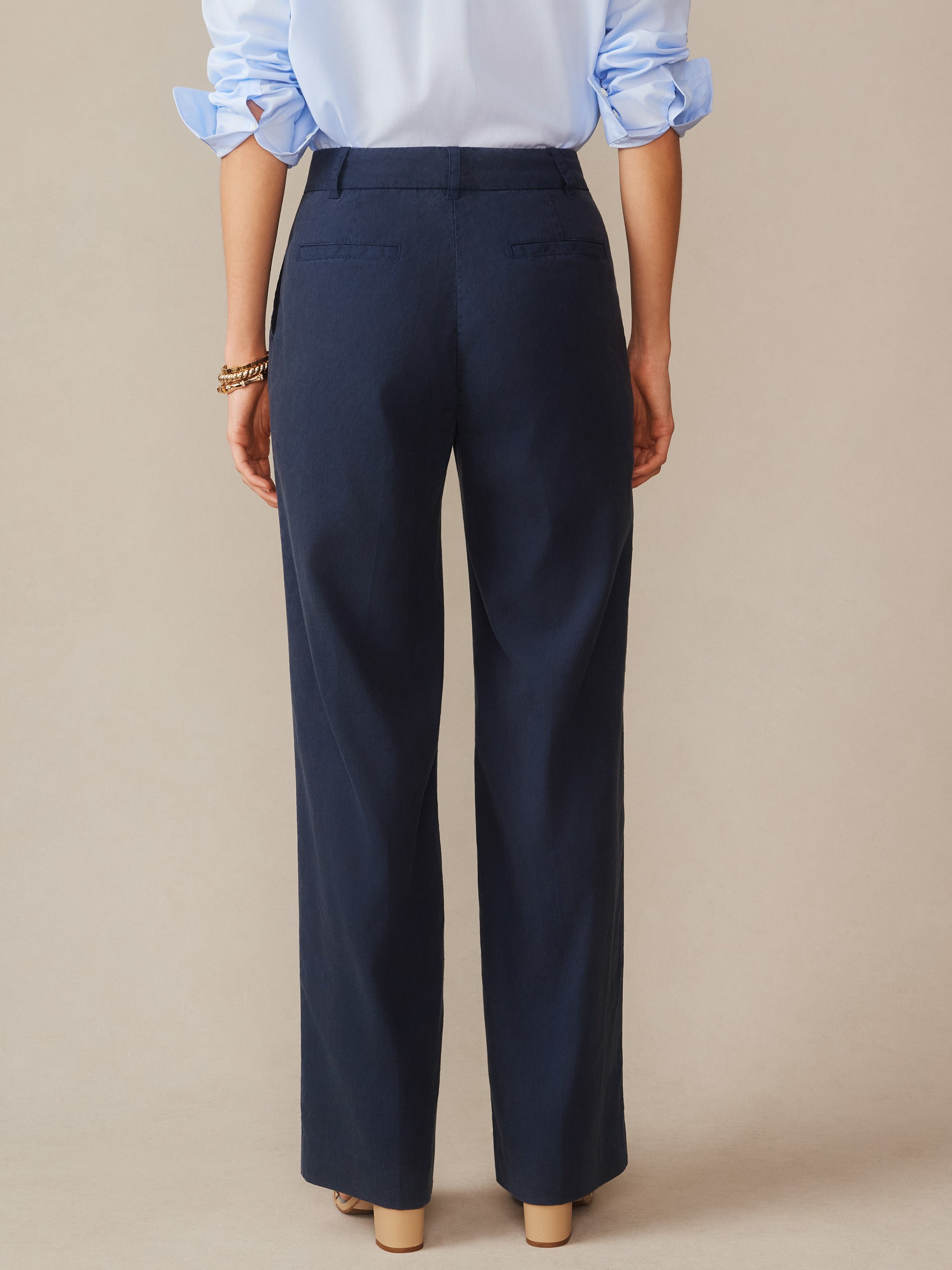 A woman wearing navy Fiona Linen Blend Pants by J.McLaughlin, paired with a light blue shirt, showcasing effortlessly stylish, enduring designs and innovative fabrics that embody a legacy of timeless fashion.