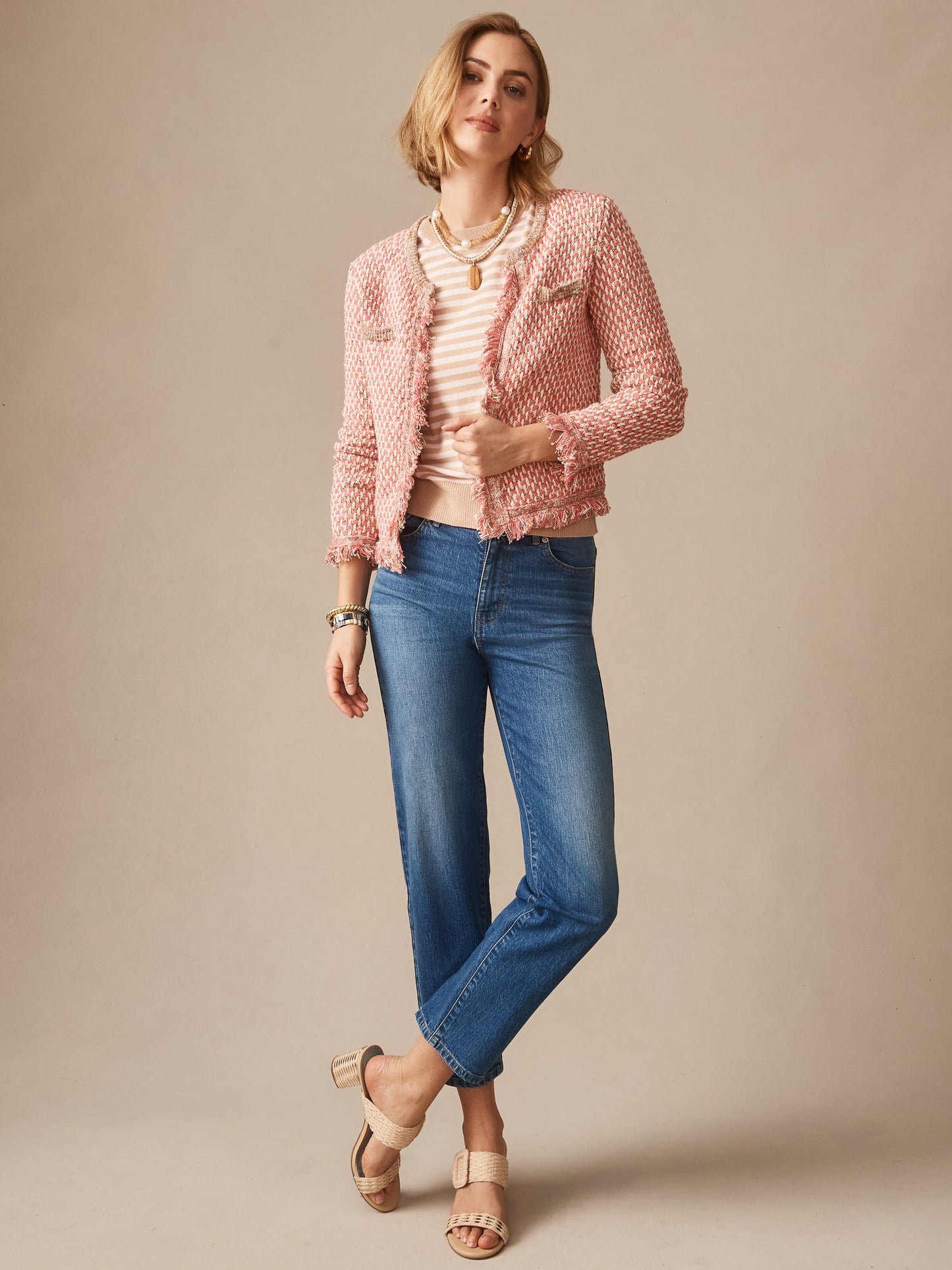 Woman wearing a pink textured Marceline Cardigan by J.McLaughlin over a light striped top with blue jeans and beige sandals, showcasing effortlessly stylish, enduring designs and innovative fabrics.