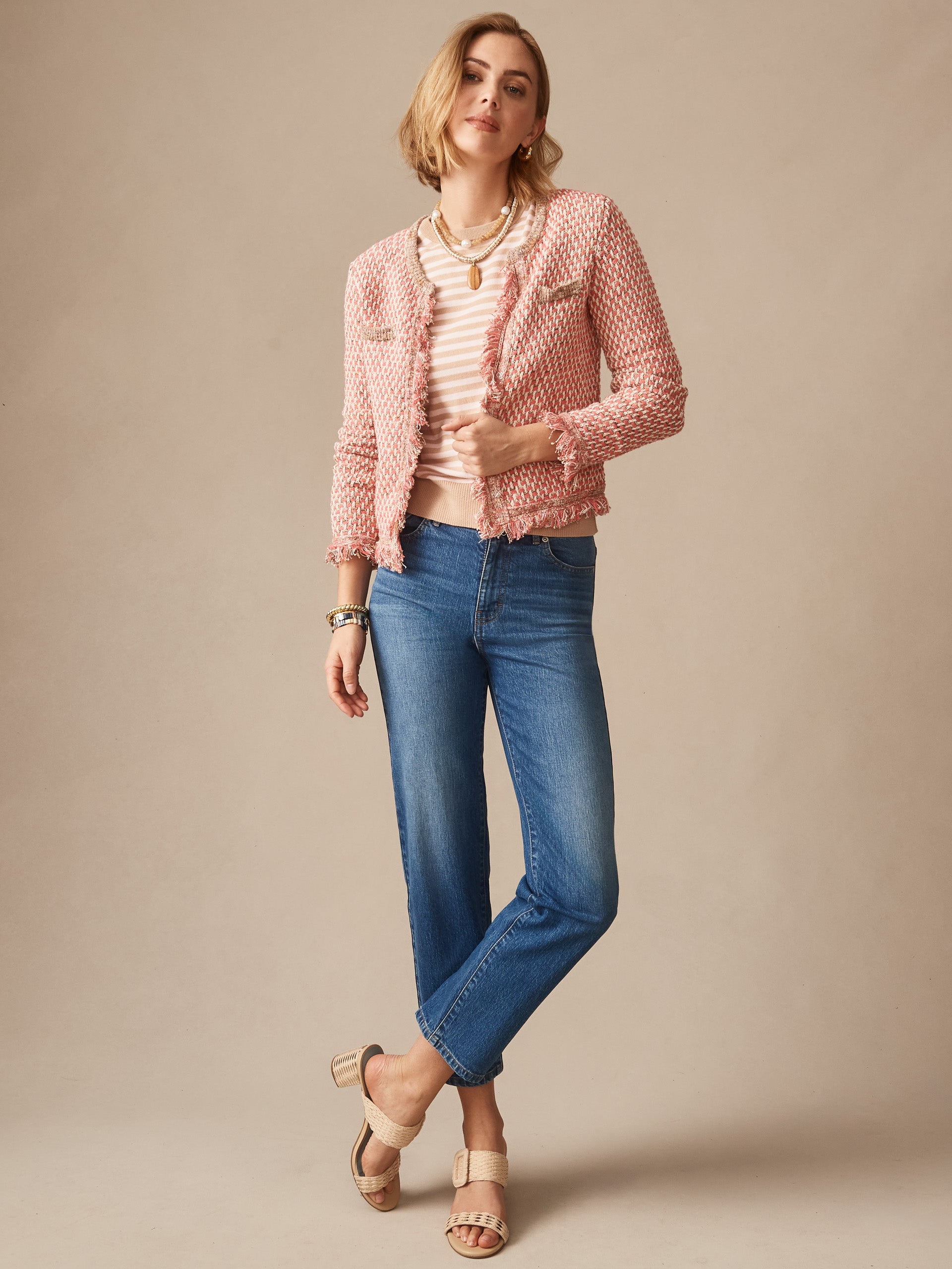 Woman wearing a pink textured Marceline Cardigan by J.McLaughlin over a light striped top with blue jeans and beige sandals, showcasing effortlessly stylish, enduring designs and innovative fabrics.