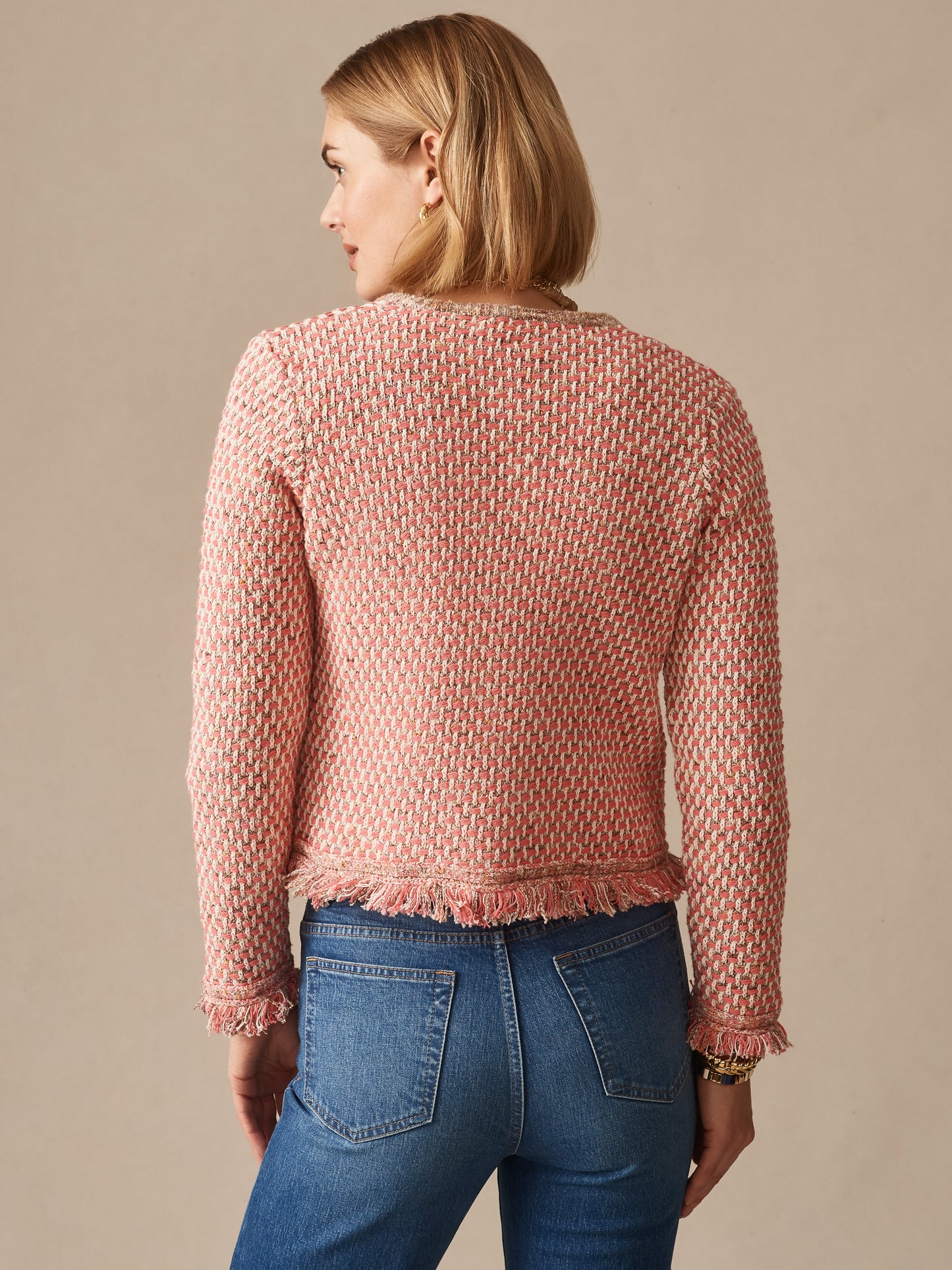 Woman wearing a pink and tan textured Marceline Cardigan by J.McLaughlin paired with blue jeans, showcasing effortlessly stylish, enduring designs and a legacy of timeless fashion.