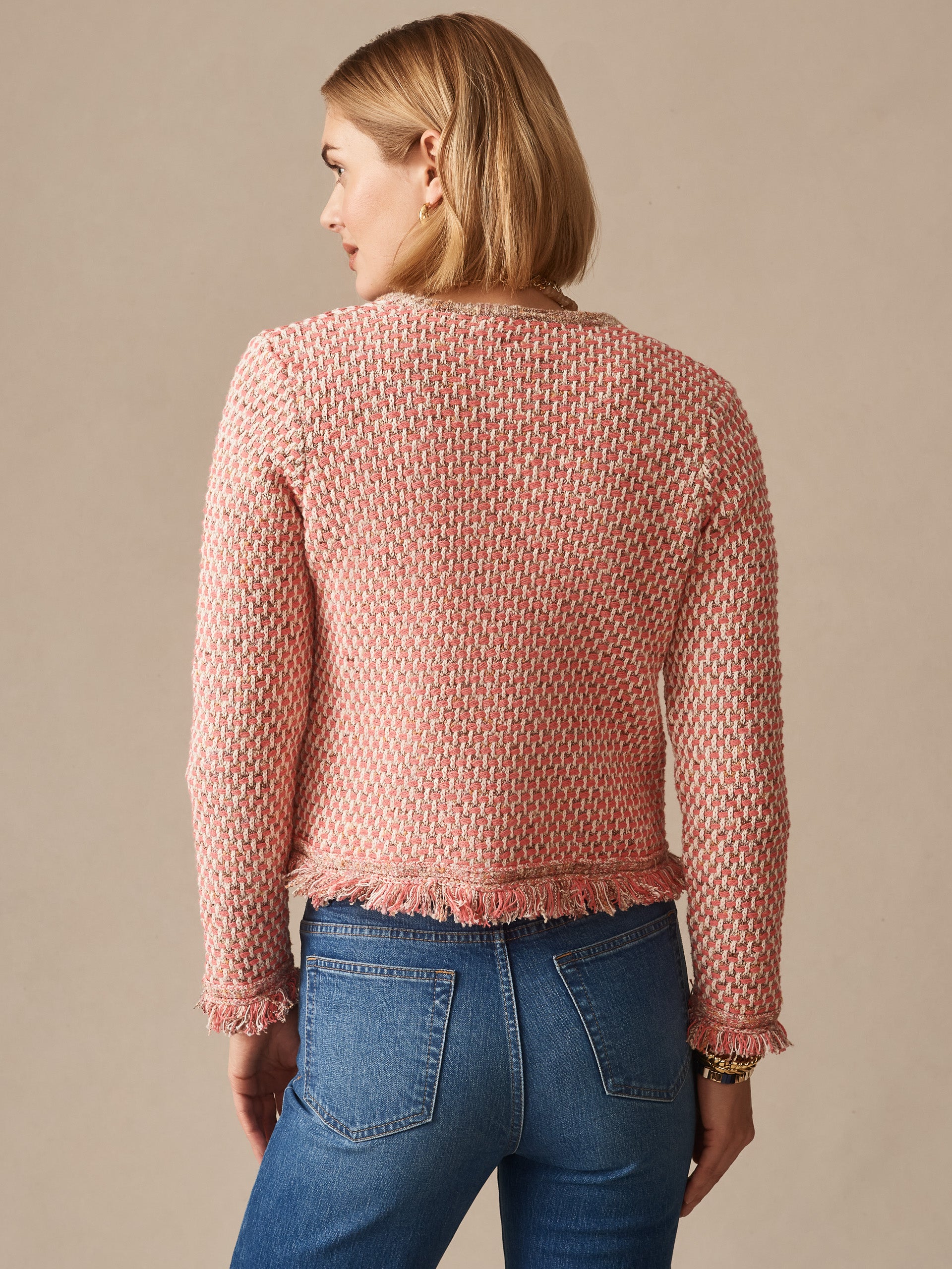 Woman wearing a pink and tan textured Marceline Cardigan by J.McLaughlin paired with blue jeans, showcasing effortlessly stylish, enduring designs and a legacy of timeless fashion.