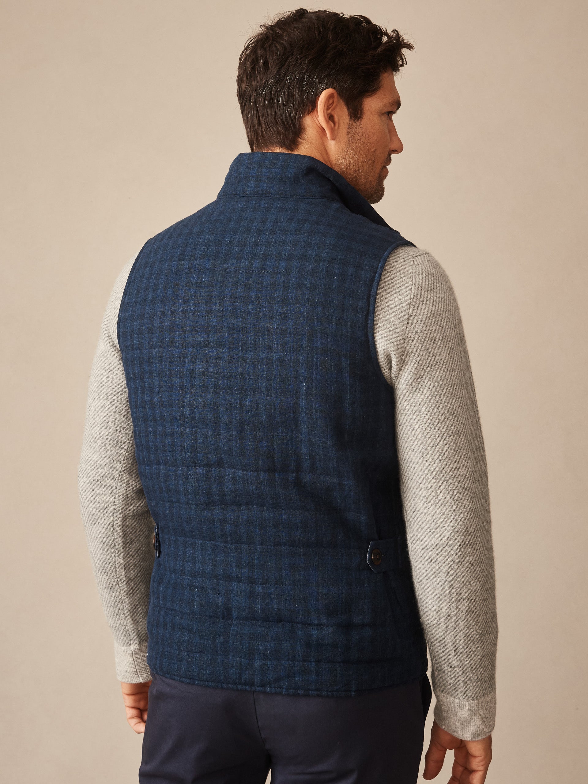 Man wearing a navy quilted vest with shadow plaid pattern over a light gray textured sweater, showcasing the back view of the Game Quilted Vest in Shadow Plaid by J.McLaughlin.
