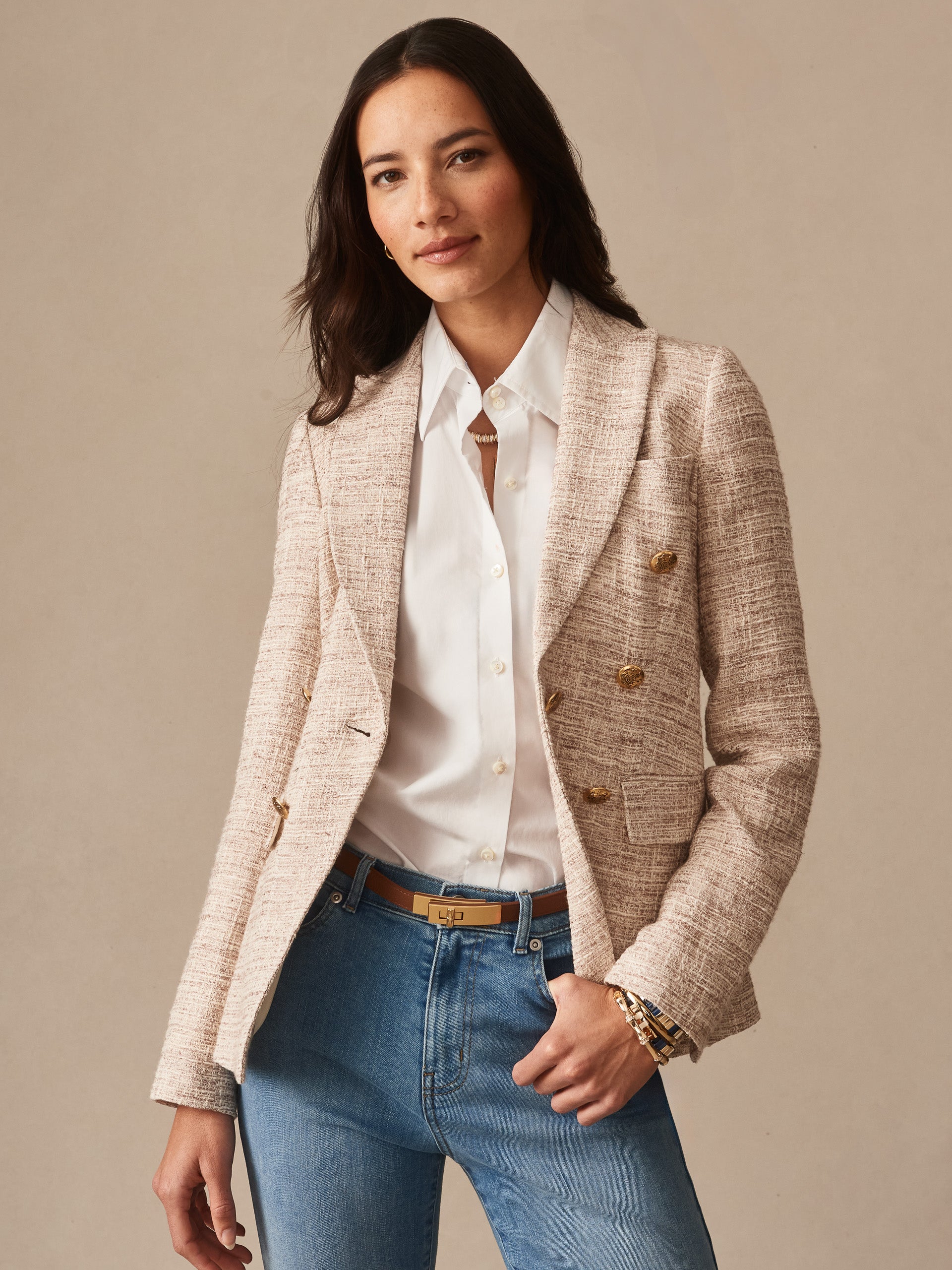 Woman wearing a light tan textured Genevieve Tweed Blazer by J.McLaughlin over a white blouse and blue jeans, styled with a neutral belt and bracelets for a classic, polished look.