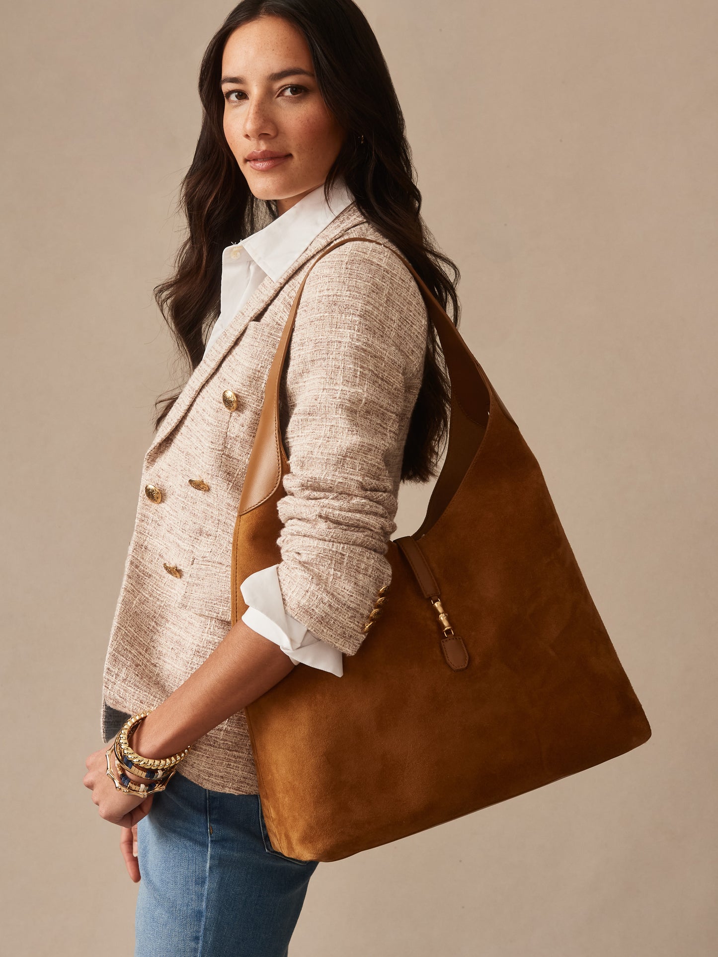 Woman wearing a light textured blazer and jeans carrying a tan Jenna Suede Tote by J.McLaughlin, showcasing effortlessly stylish bags crafted with enduring designs and innovative fabrics.