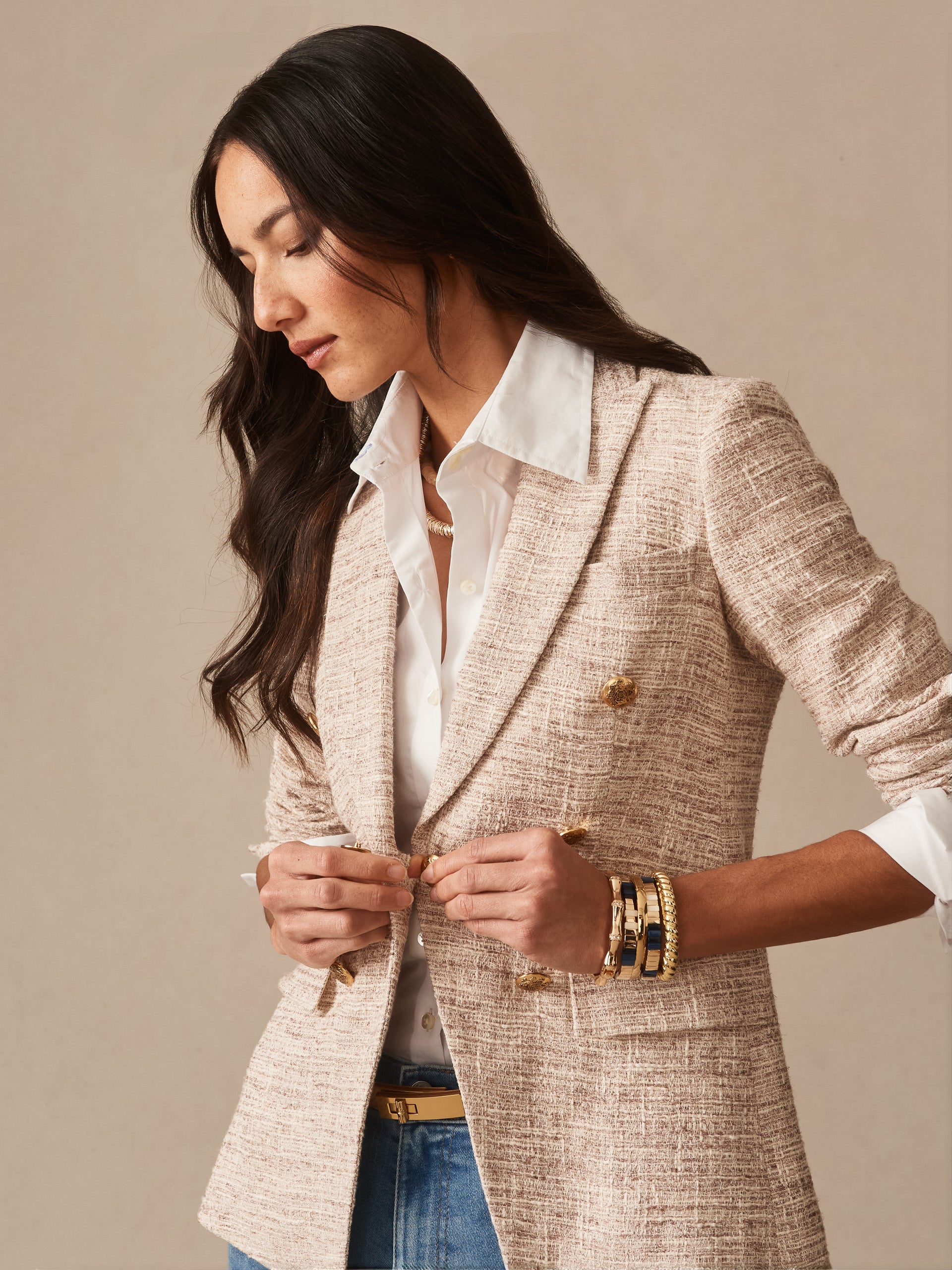 Woman wearing a cream and tan textured Genevieve Tweed Blazer by J.McLaughlin over a white collared shirt, accessorized with gold bracelets and a belt, highlighting classic style.