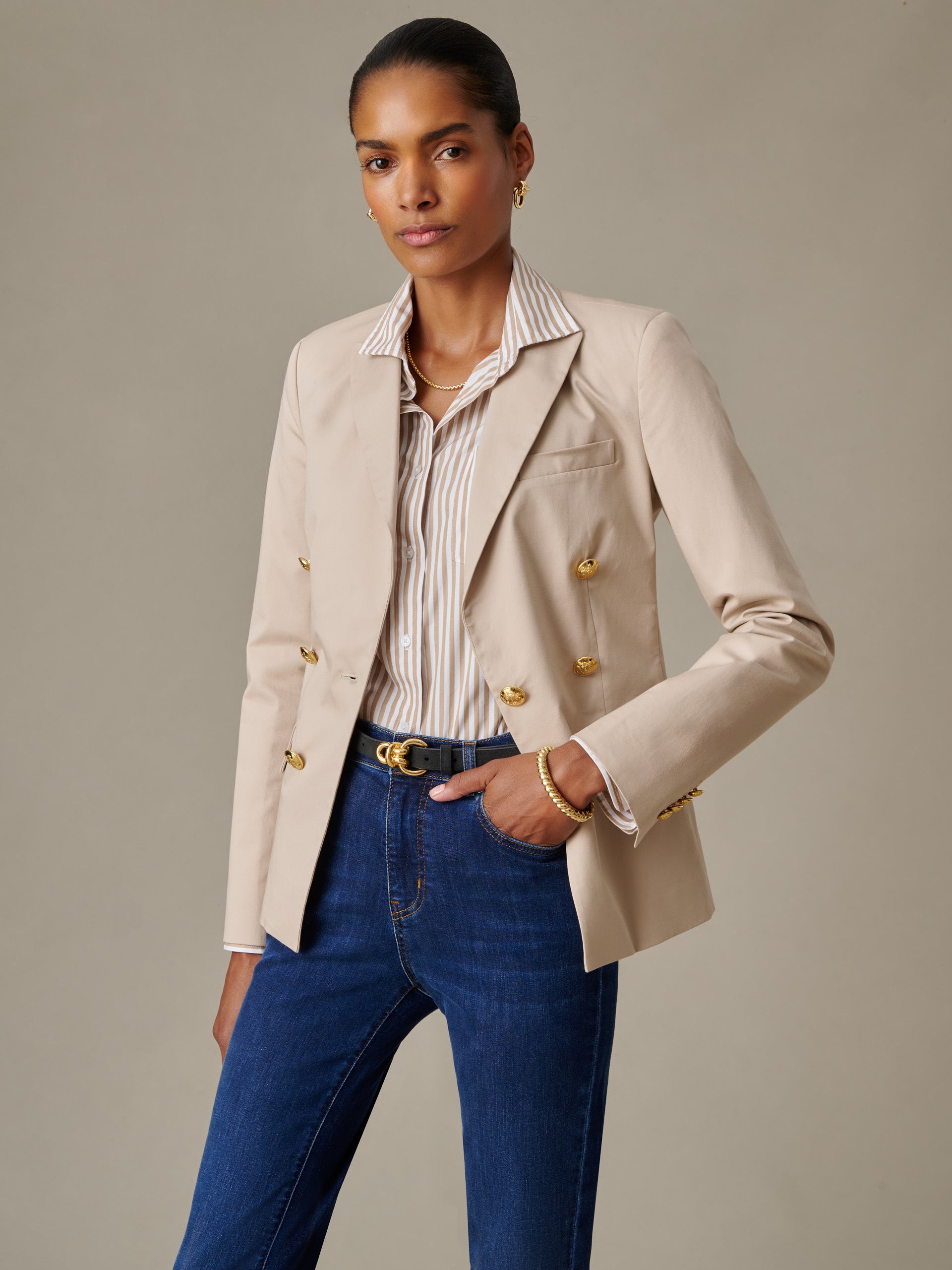 Woman wearing a beige Genevieve Cotton Twill Blazer by J.McLaughlin paired with a striped blouse and dark blue jeans, showcasing effortlessly stylish and enduring design.