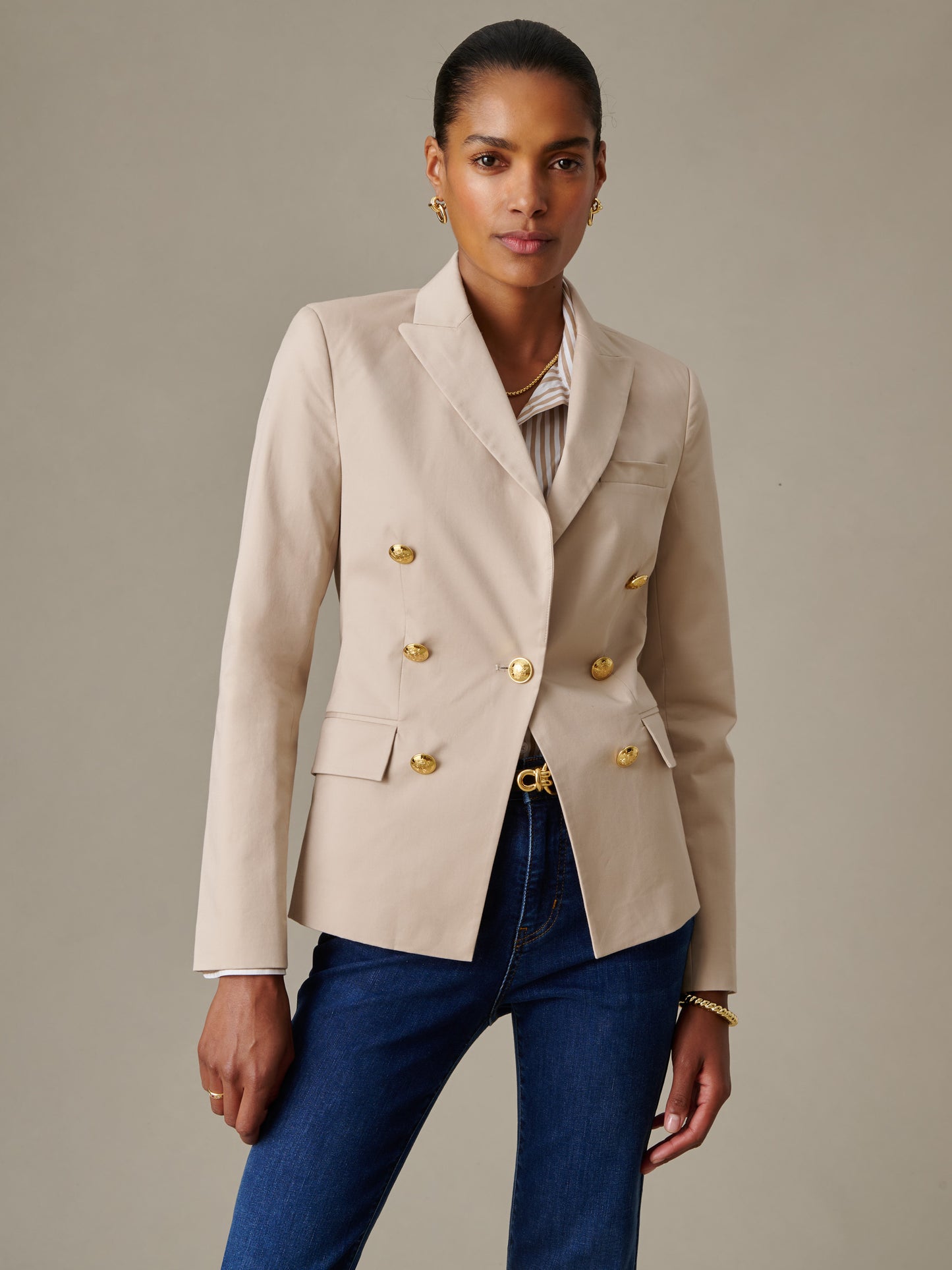 Woman wearing a Genevieve Cotton Twill Blazer by J.McLaughlin in beige with gold buttons, paired with dark blue jeans and subtle gold jewelry, showcasing timeless style.