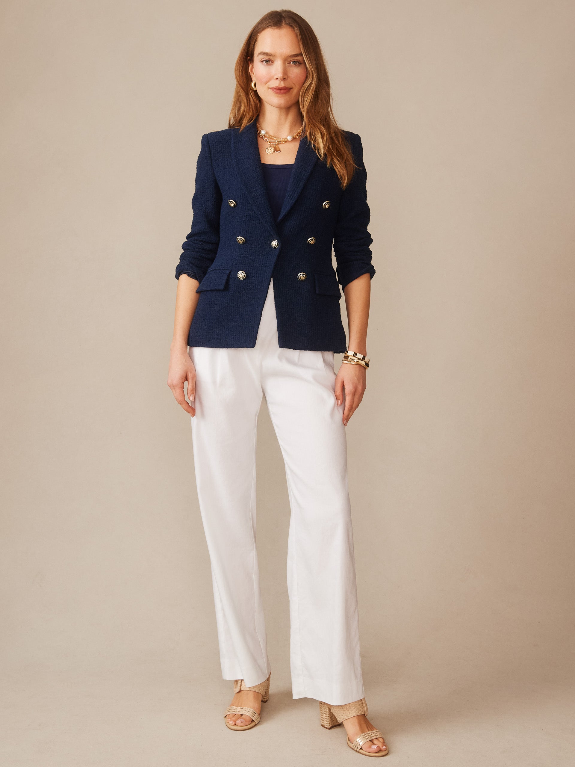 Woman wearing a navy Genevieve Cotton Bouclé Blazer by J.McLaughlin paired with white pants and sandals, showcasing effortlessly stylish, enduring designs in a legacy of timeless fashion.