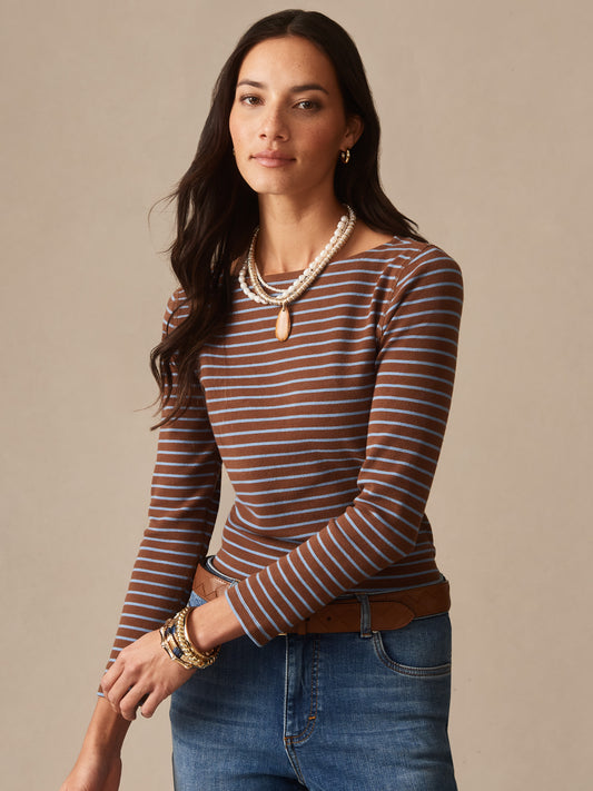 Woman wearing a brown and light blue striped Goldie Tee in Stripe by J.McLaughlin paired with denim jeans and layered beaded necklaces, showcasing effortlessly stylish, enduring designs with innovative fabrics. A destination for defining style. Life, Well-Lived.