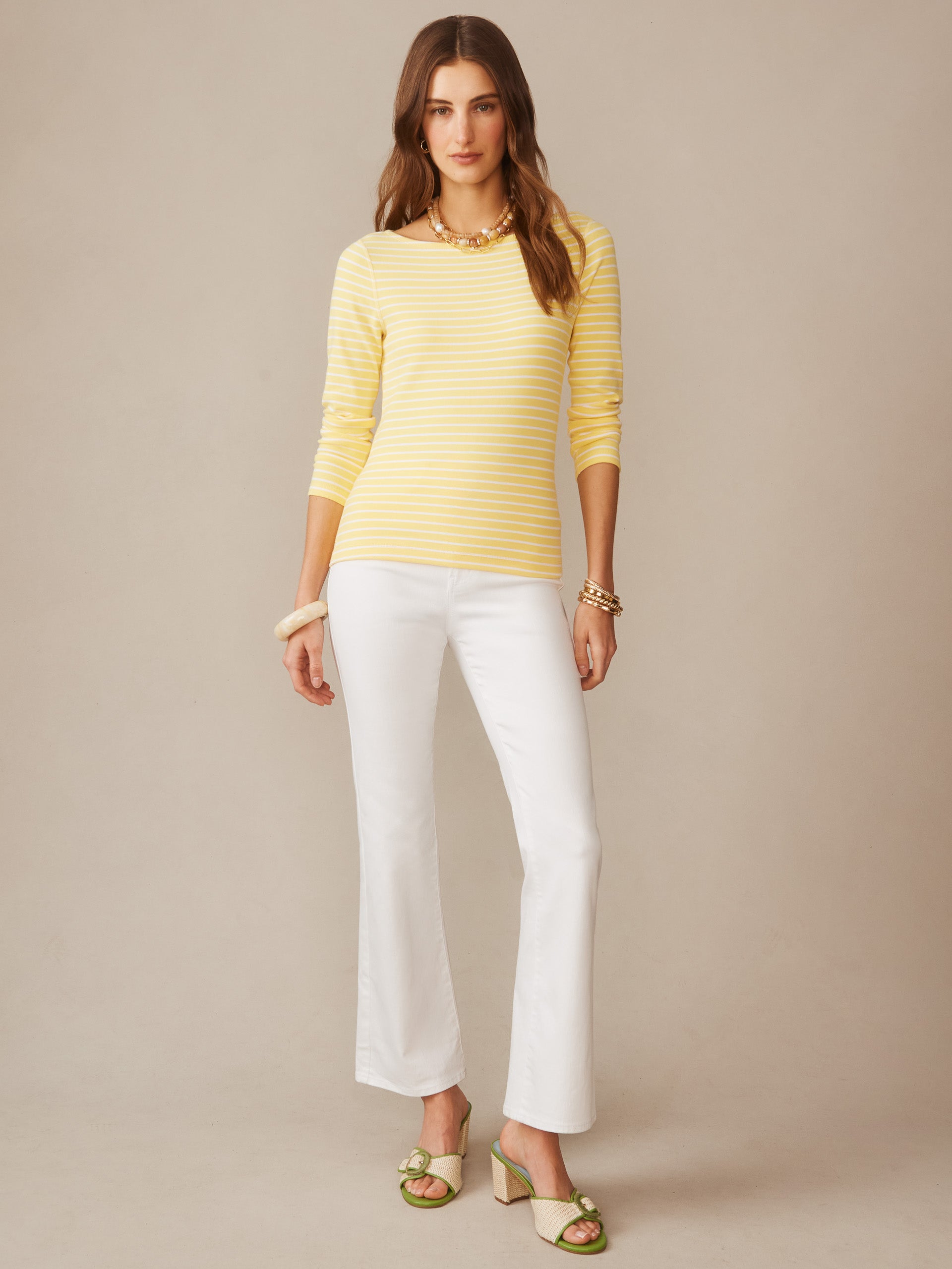 A model wearing the Goldie Tee in Stripe by J.McLaughlin, featuring effortlessly stylish yellow and white stripes, paired with white pants and green heeled sandals, showcasing enduring designs and innovative fabrics for a legacy of timeless fashion at a destination for defining style. Life, Well-Lived.