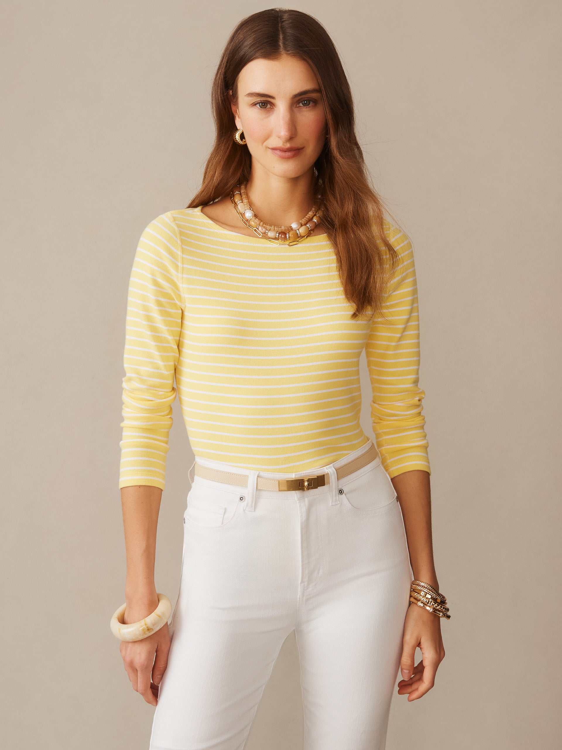 Woman wearing a yellow and white striped Goldie Tee in Stripe from J.McLaughlin paired with white pants and gold accessories, showcasing effortlessly stylish, enduring designs in innovative fabrics.