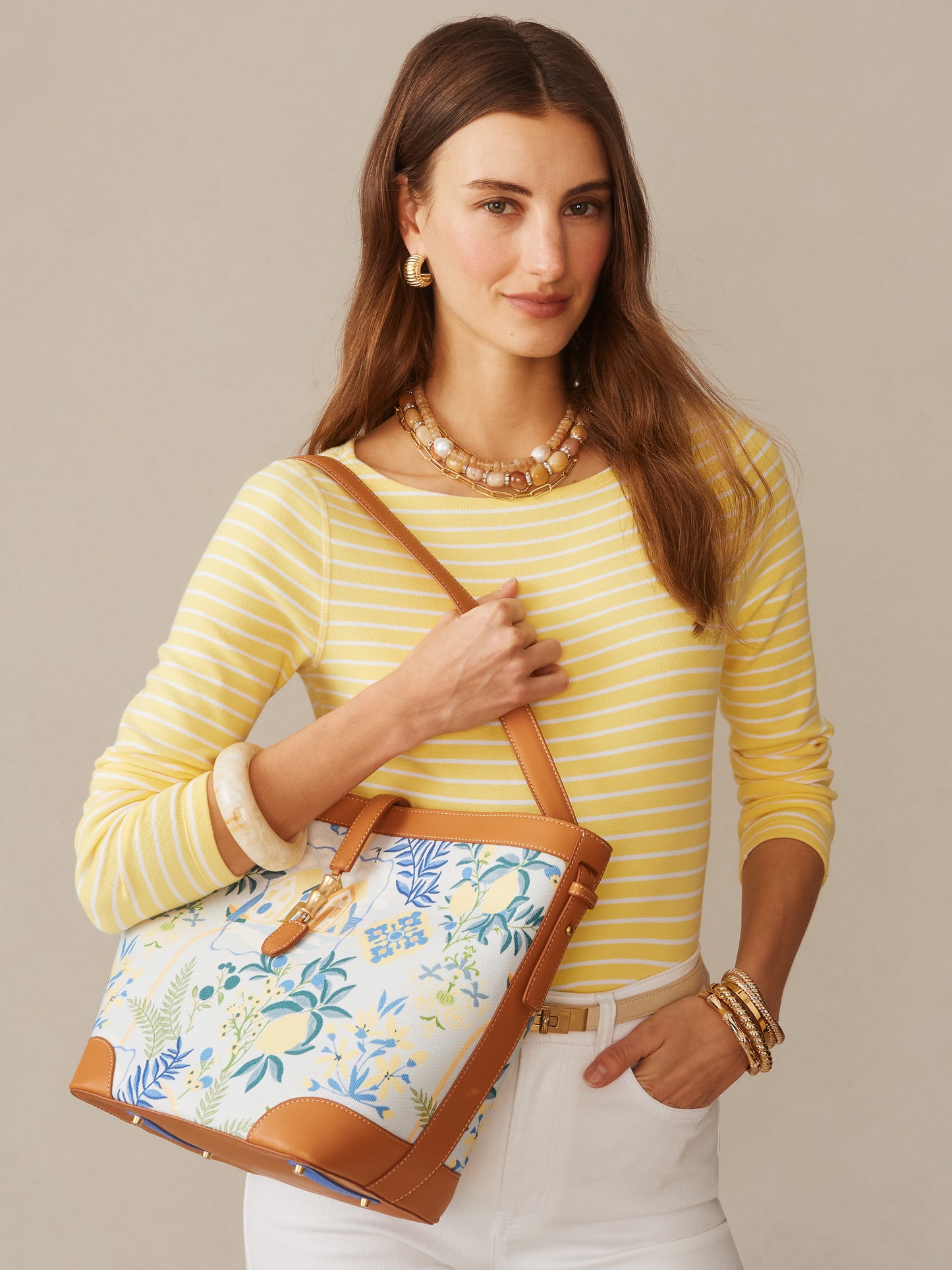 Woman wearing yellow striped top and white pants, carrying a Crawford Handbag in Amalfi Coast by J.McLaughlin, showcasing effortlessly stylish bags with enduring designs and innovative fabrics.