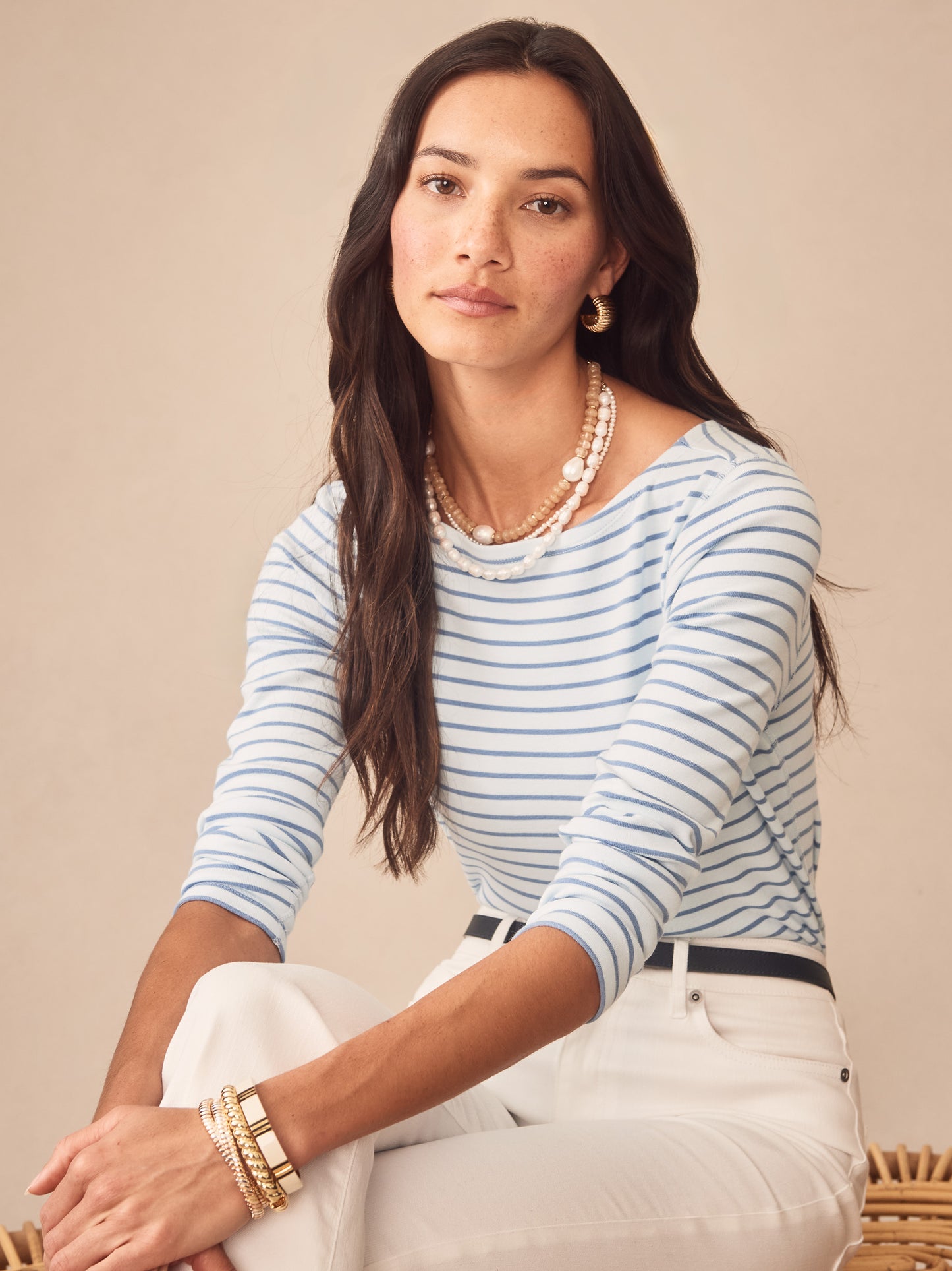 Woman wearing the Goldie Tee in Stripe by J.McLaughlin, featuring soft blue stripes and a classic fit, paired with white pants and layered pearl necklaces, embodying effortlessly stylish and enduring designs in innovative fabrics for a legacy of timeless fashion at a destination for defining style. Life, Well-Lived.
