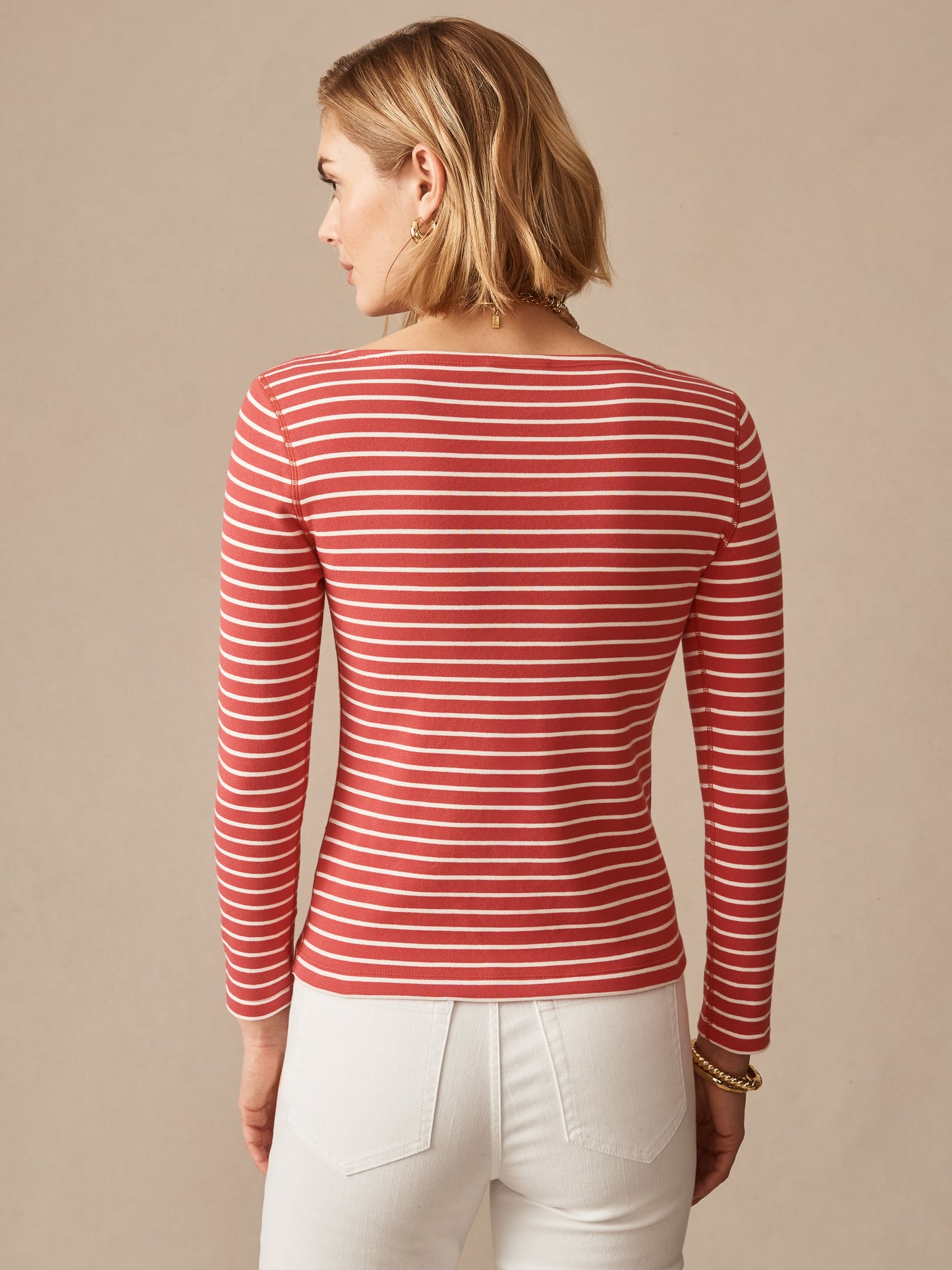 Woman wearing a striped long-sleeve tee in coral and cream, paired with white pants, showcasing the Goldie Tee in Stripe by J.McLaughlin, representing effortlessly stylish, enduring designs with innovative fabrics for a legacy of timeless fashion. A destination for defining style. Life, Well-Lived.
