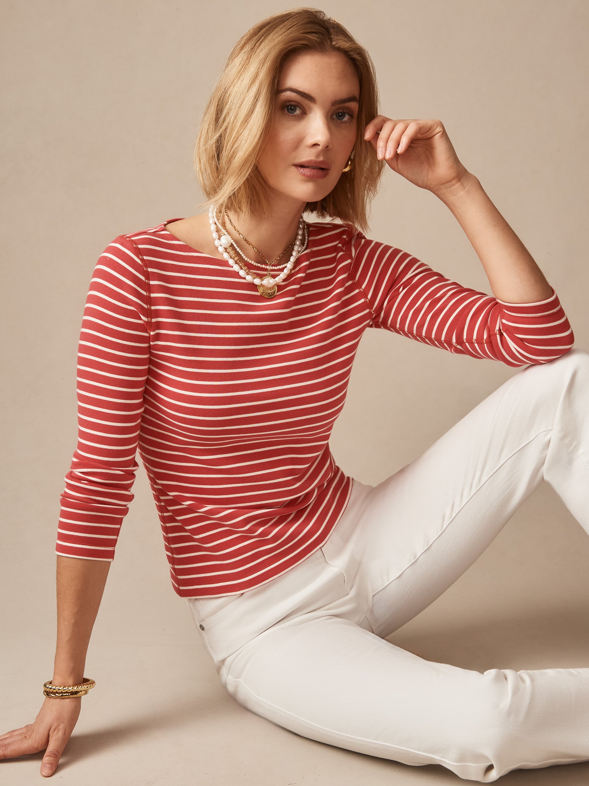 Woman wearing a coral and cream striped Goldie Tee in Stripe by J.McLaughlin paired with white pants, showcasing effortlessly stylish design and enduring appeal for a destination defining style. Life, Well-Lived.