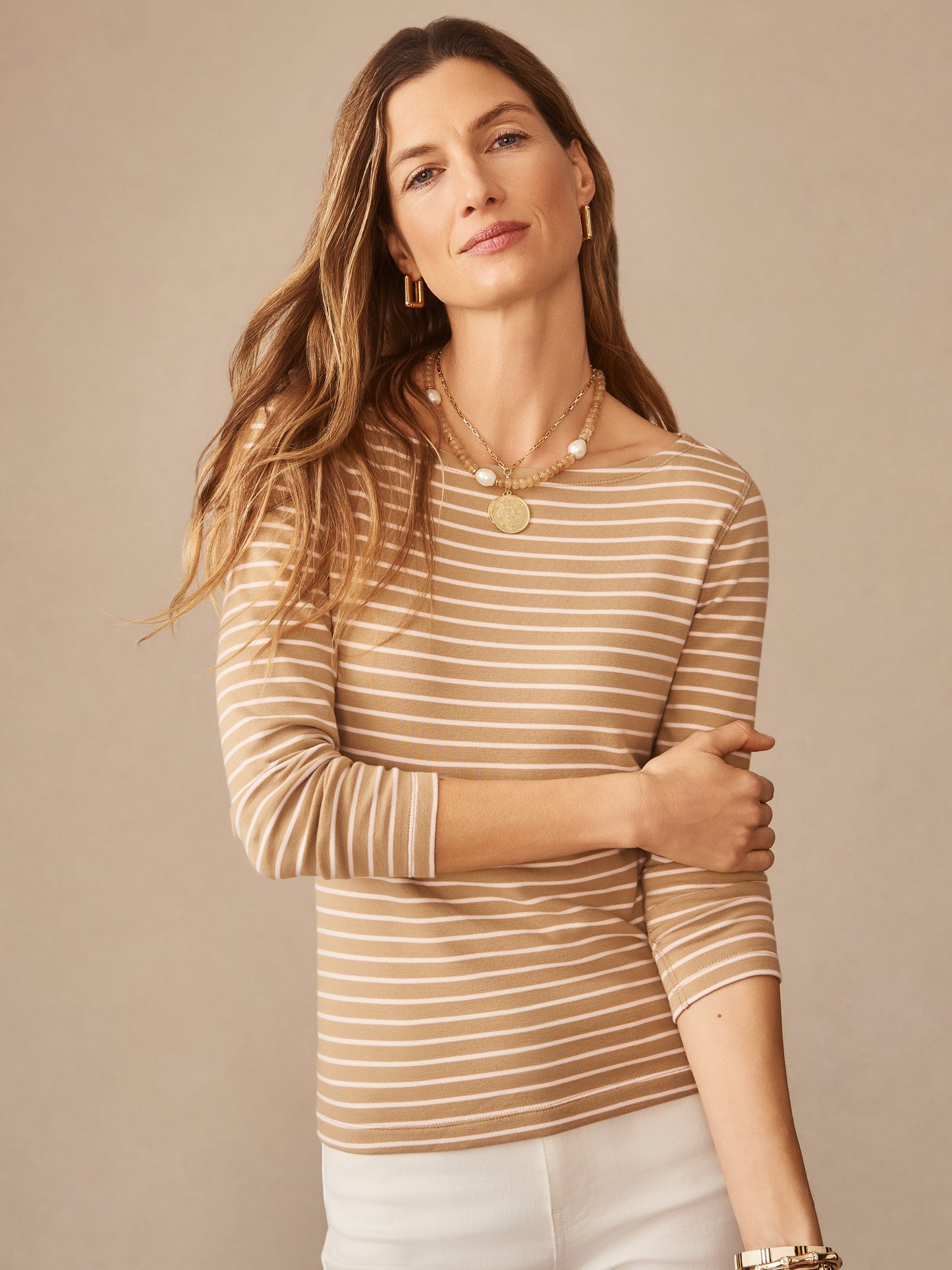 Woman wearing J.McLaughlin Goldie Tee in Stripe with beige and white horizontal stripes, paired with layered necklaces, embodying effortlessly stylish and enduring designs for a life well-lived.