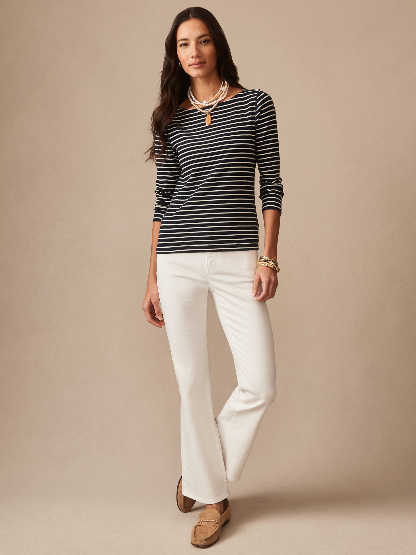 Woman wearing a navy and cream striped Goldie Tee in Stripe paired with white pants and loafers, embodying effortlessly stylish, enduring designs by J.McLaughlin, a destination for defining style. Life, Well-Lived.