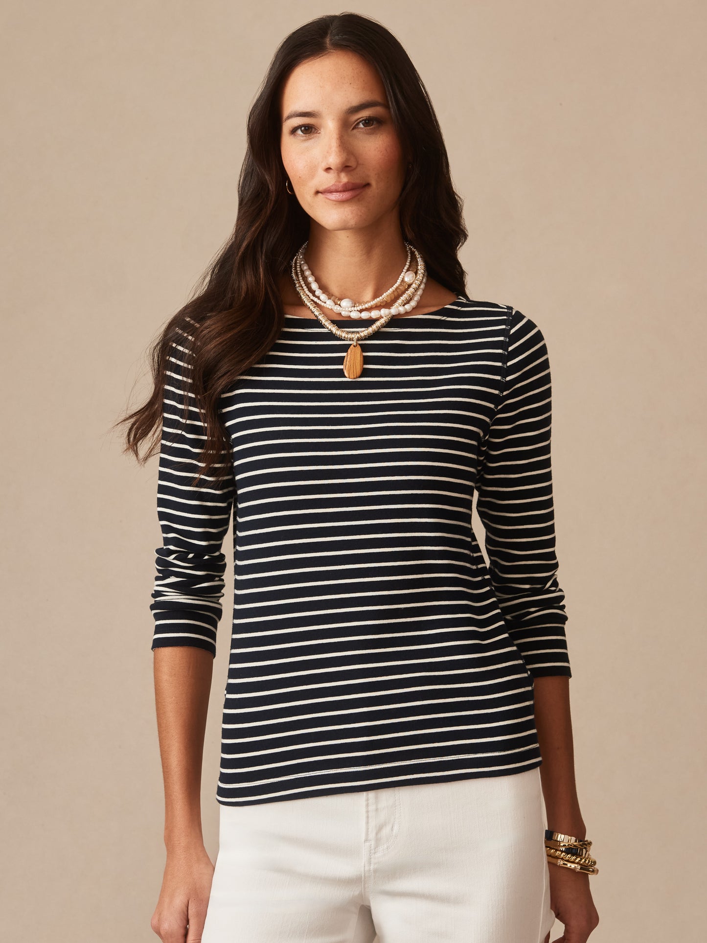 A woman wearing the Goldie Tee in Stripe by J.McLaughlin, featuring navy and cream stripes, styled with layered necklaces and bracelets, embodying effortlessly stylish, enduring designs and innovative fabrics at a destination for defining style. Life, Well-Lived.