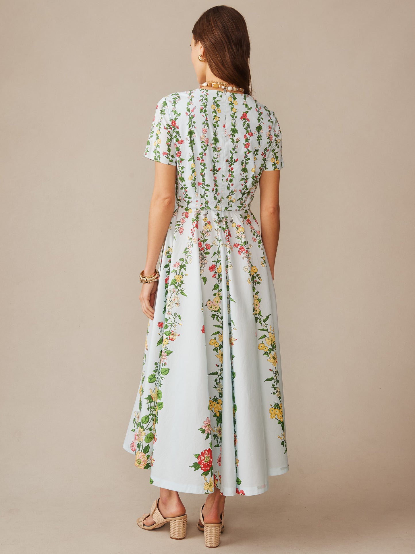 A woman wearing the Grace Dress in Floral Medley Ray by J.McLaughlin, featuring a flowing silhouette with vertical floral patterns on a light blue background, embodying effortlessly stylish and enduring designs. A destination for defining style. Life, Well-Lived.