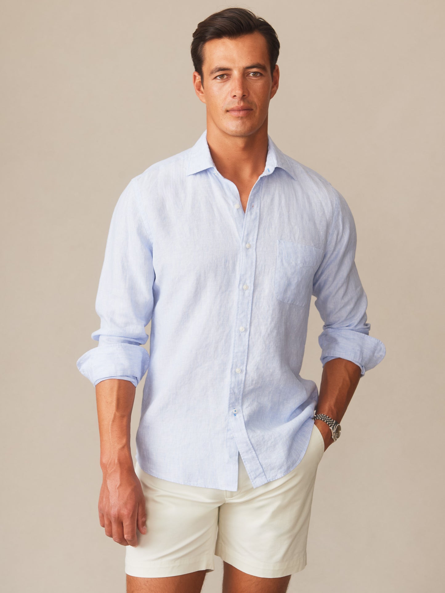 Man wearing a light blue Gramercy Linen Shirt in Hairline Stripe by J.McLaughlin paired with white shorts, showcasing effortlessly stylish design and enduring craftsmanship, a destination for defining style. Life, Well-Lived.