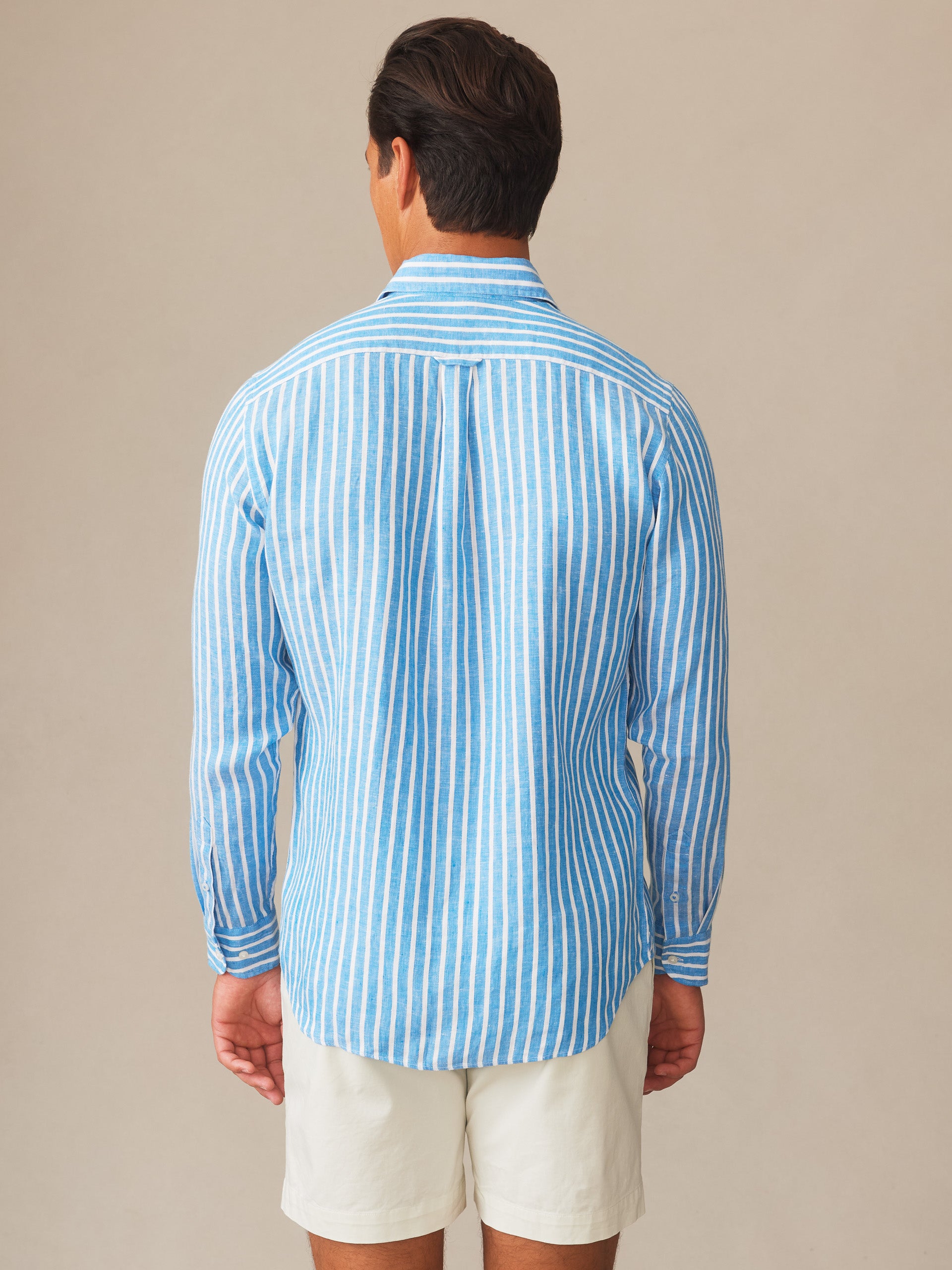 Man wearing a Gramercy Linen Shirt in Dobby Stripe by J.McLaughlin, featuring blue and white vertical stripes, showcasing effortlessly stylish, enduring designs with innovative fabrics, embodying a legacy of timeless fashion. A destination for defining style. Life, Well-Lived.