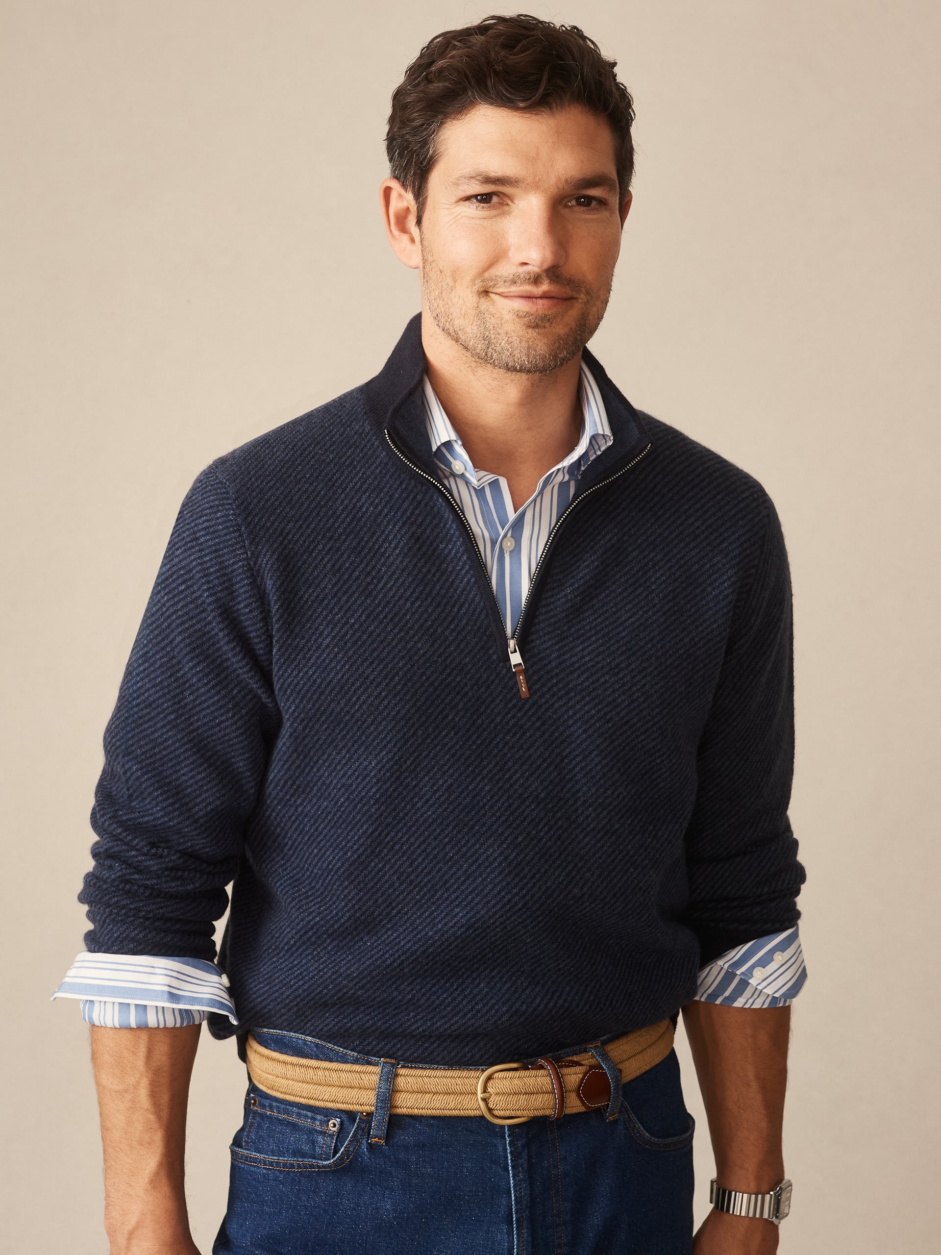 Man wearing a navy blue Twain Cashmere 1/4 Zip in Jacquard sweater over a striped shirt with rolled sleeves, styled with jeans and a tan belt, showcasing J.McLaughlin’s effortlessly stylish and enduring designs.