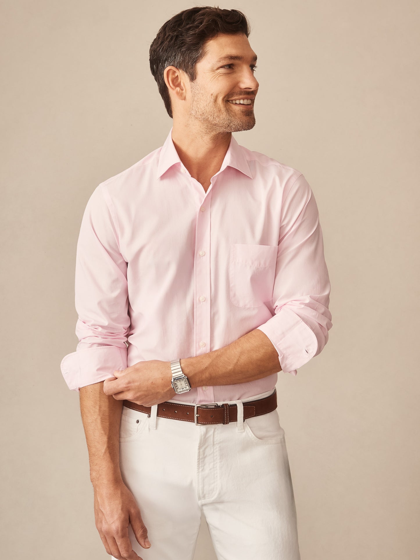 A smiling man wearing a light pink Gramercy Cotton Shirt by J.McLaughlin with rolled-up sleeves, paired with white pants and a brown belt, showcasing classic style and craftsmanship.