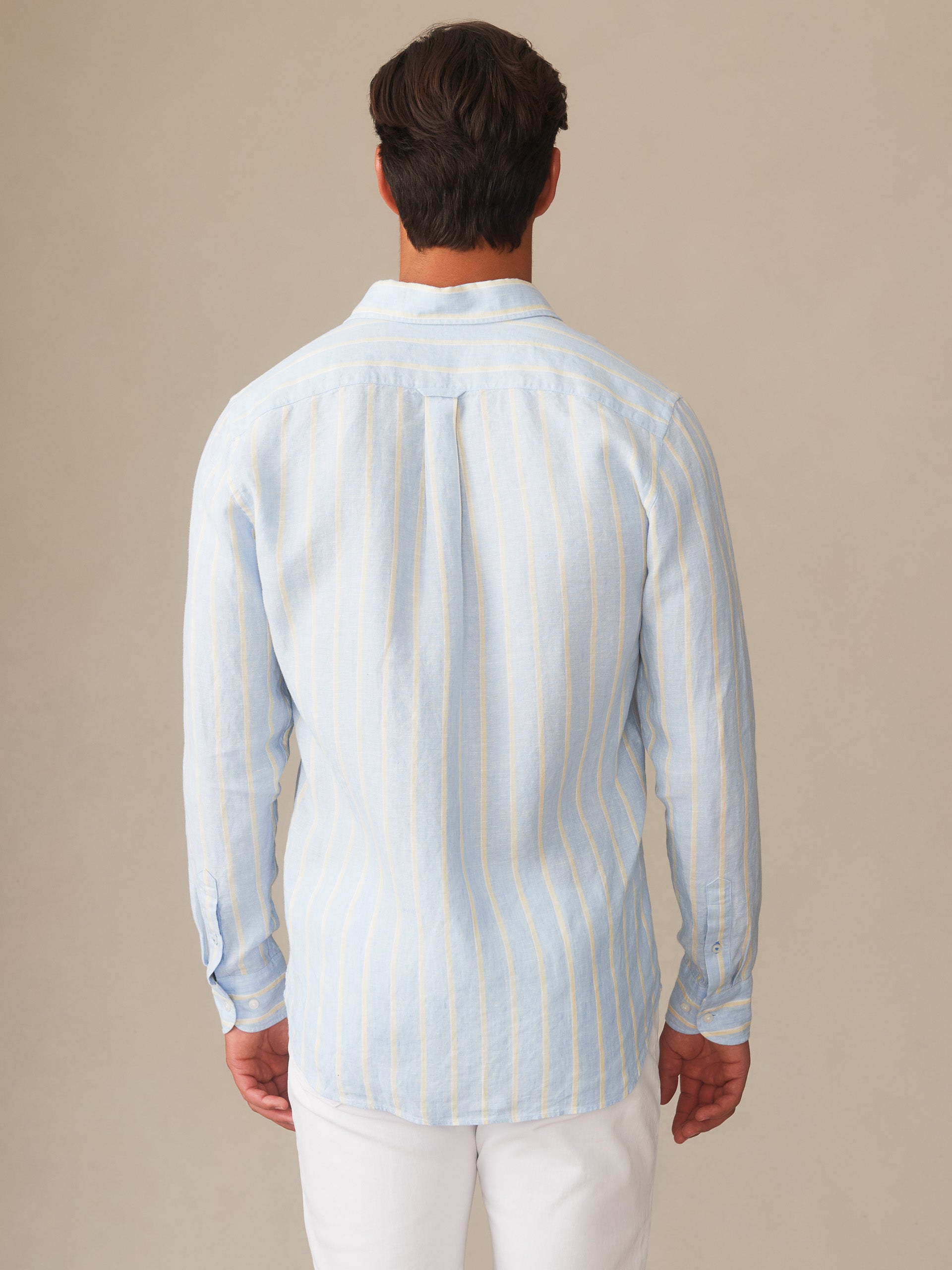 A man wears the Gramercy Linen Shirt in Dobby Stripe by J.McLaughlin, showcasing effortlessly stylish, enduring designs and innovative fabrics for a legacy of timeless fashion.