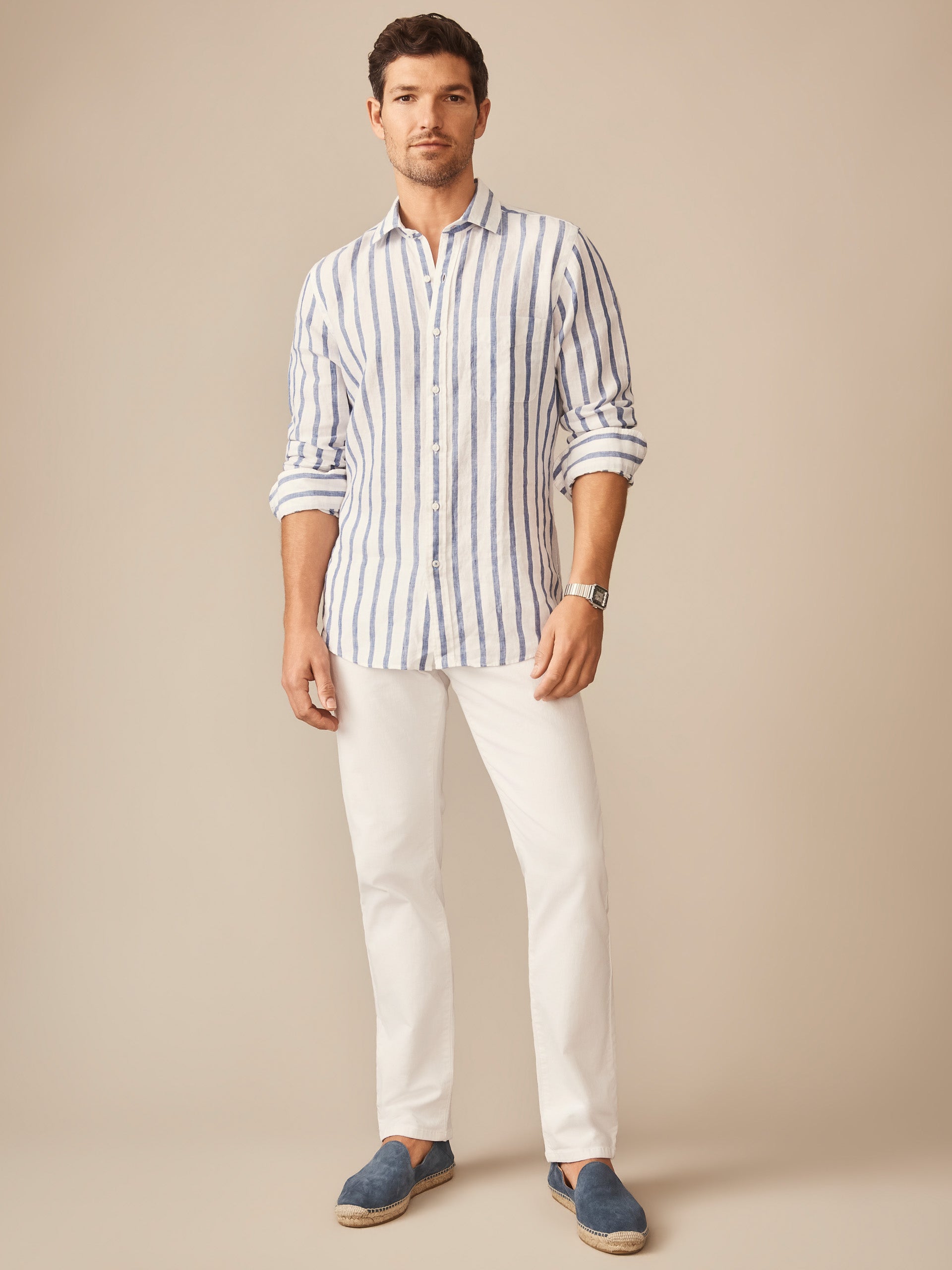 A man wearing the Gramercy Linen Shirt in Dobby Stripe by J.McLaughlin styled with white pants and navy slip-on shoes, showcasing effortlessly stylish, enduring designs and innovative fabrics from a destination for defining style. Life, Well-Lived.