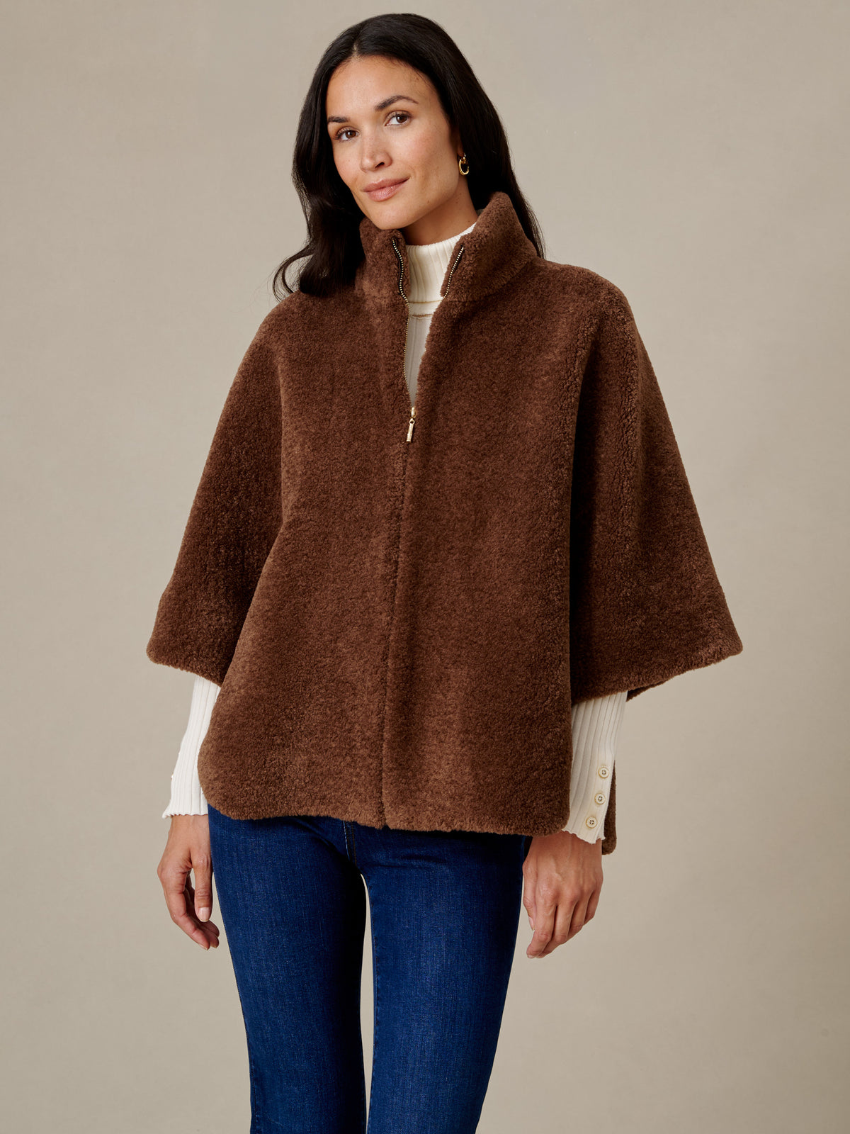 J.McLaughlin Gretchen Faux Fur Cape in brown plush faux fur with a stand collar and gold tone zipper worn over a cream sweater and blue jeans