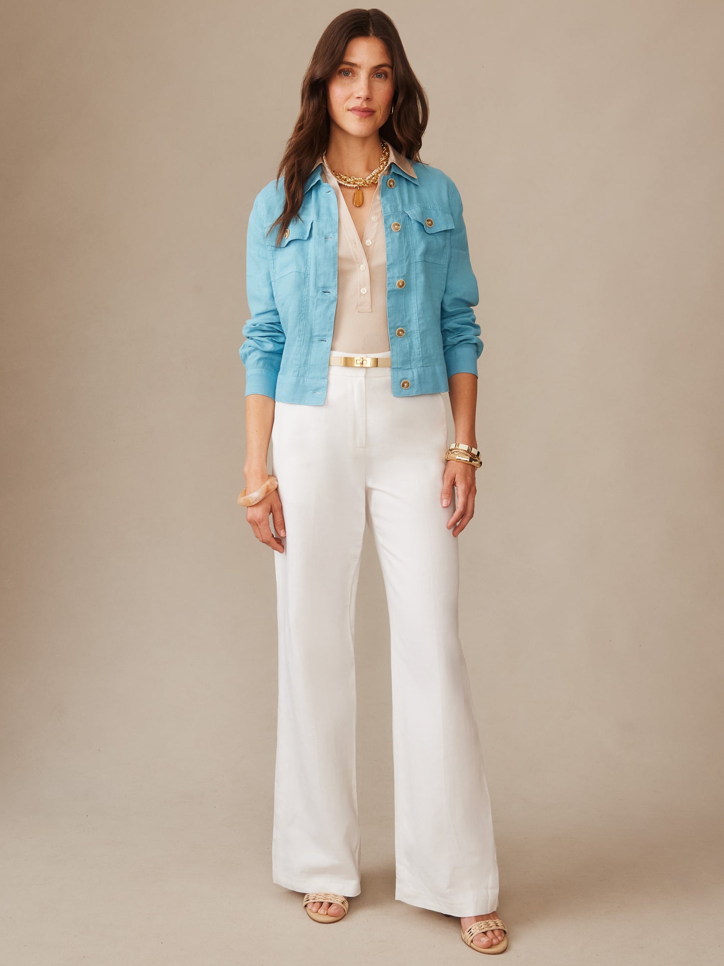 Woman wearing a teal Halo Linen Jacket by J.McLaughlin layered over a beige top with white wide-leg pants and gold accessories, showcasing effortlessly stylish, enduring designs.