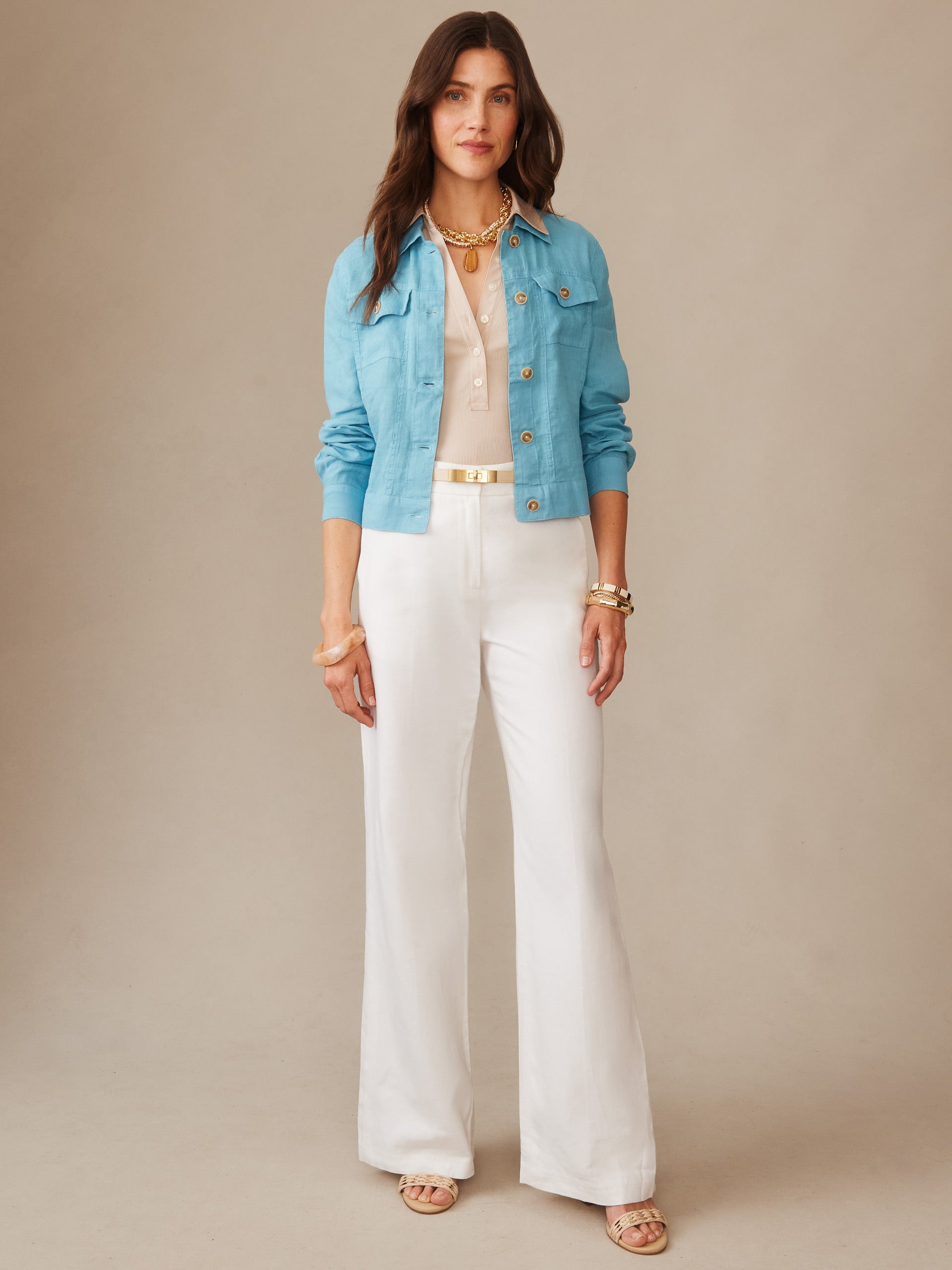 Woman wearing a teal Halo Linen Jacket by J.McLaughlin layered over a beige top with white wide-leg pants and gold accessories, showcasing effortlessly stylish, enduring designs.