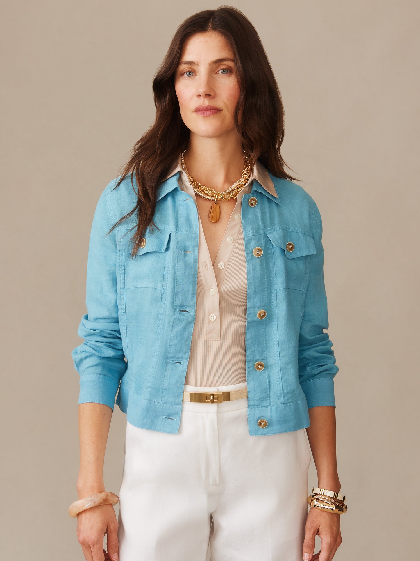 A woman wears the Halo Linen Jacket in soft blue by J.McLaughlin, styled with a beige blouse and white pants, showcasing effortlessly stylish, enduring designs with a legacy of timeless fashion.