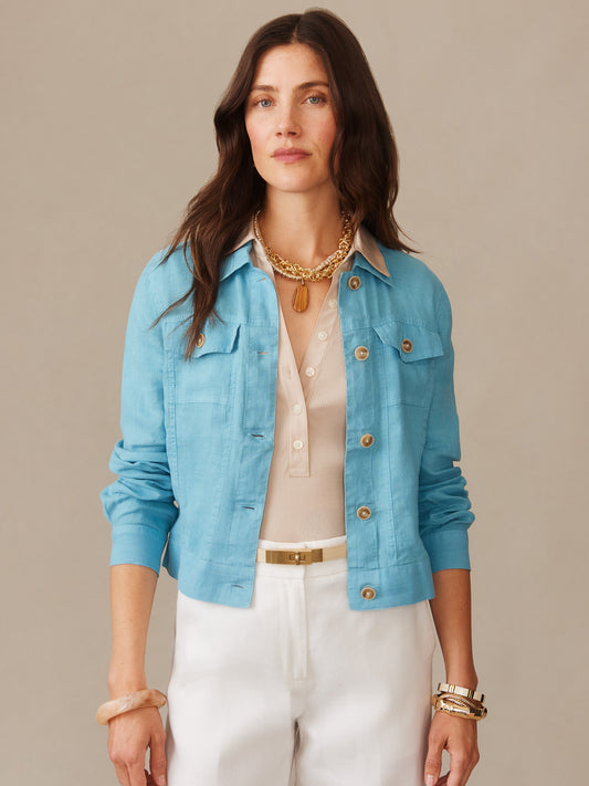 A woman wears the Halo Linen Jacket in soft blue by J.McLaughlin, styled with a beige blouse and white pants, showcasing effortlessly stylish, enduring designs with a legacy of timeless fashion.