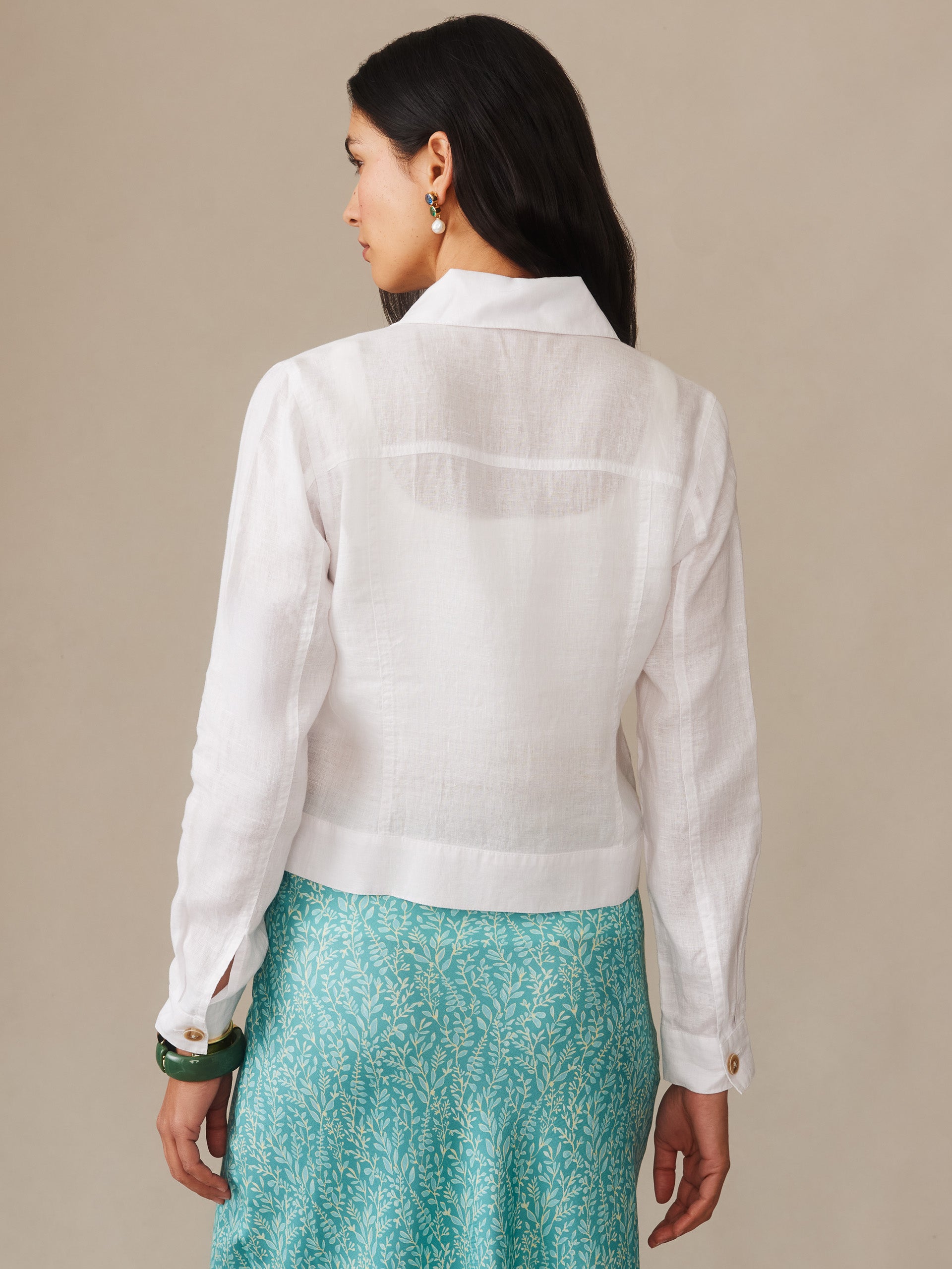 Woman wearing a white Halo Linen Jacket from J.McLaughlin paired with a turquoise patterned skirt, showcasing effortlessly stylish, enduring designs and innovative fabrics.