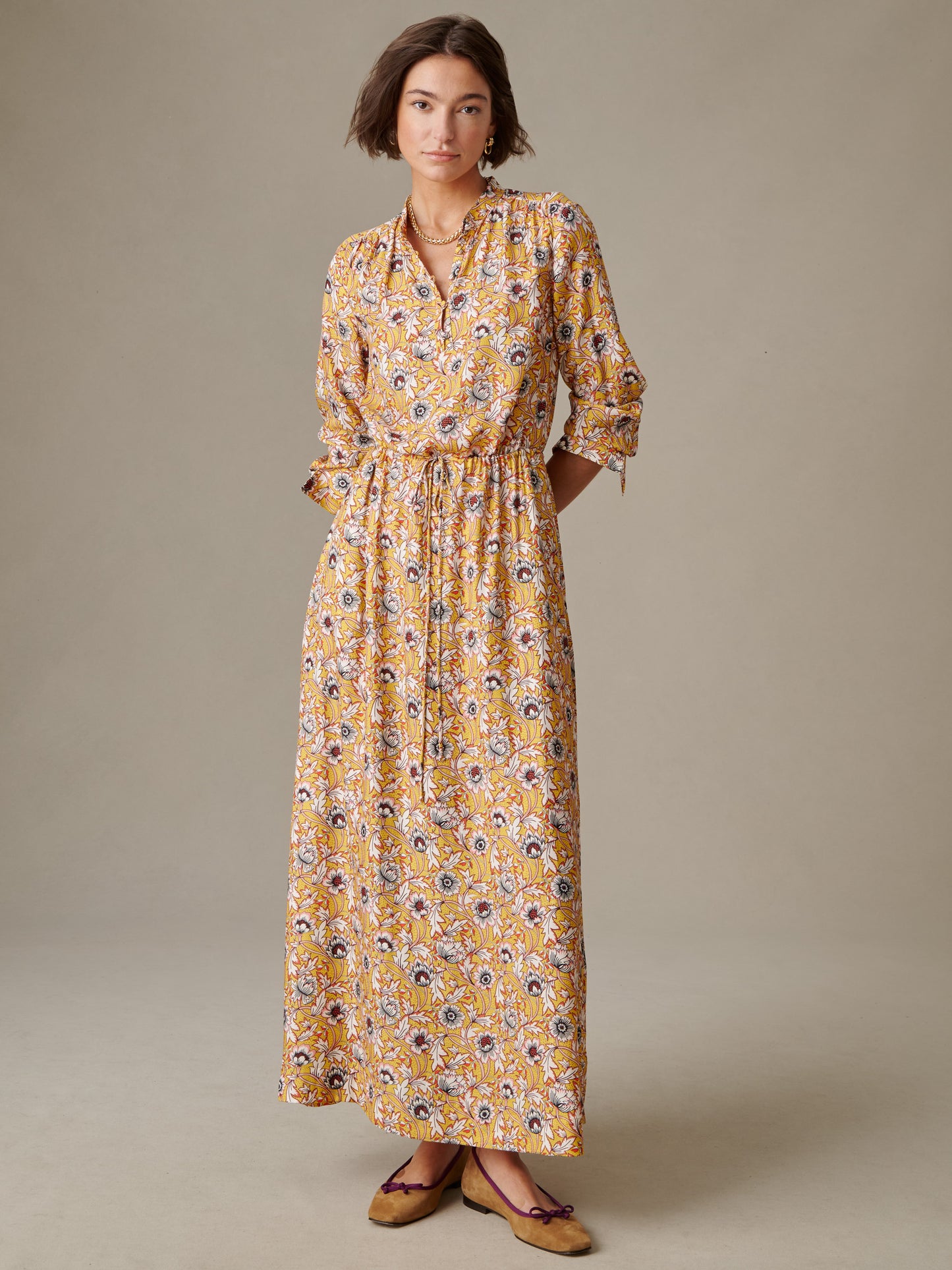 Woman modeling the Hannah Silk Blend Dress in Belle Epoque Bloom by J.McLaughlin, featuring a yellow floral pattern with long sleeves and a cinched waist, paired with brown flats.