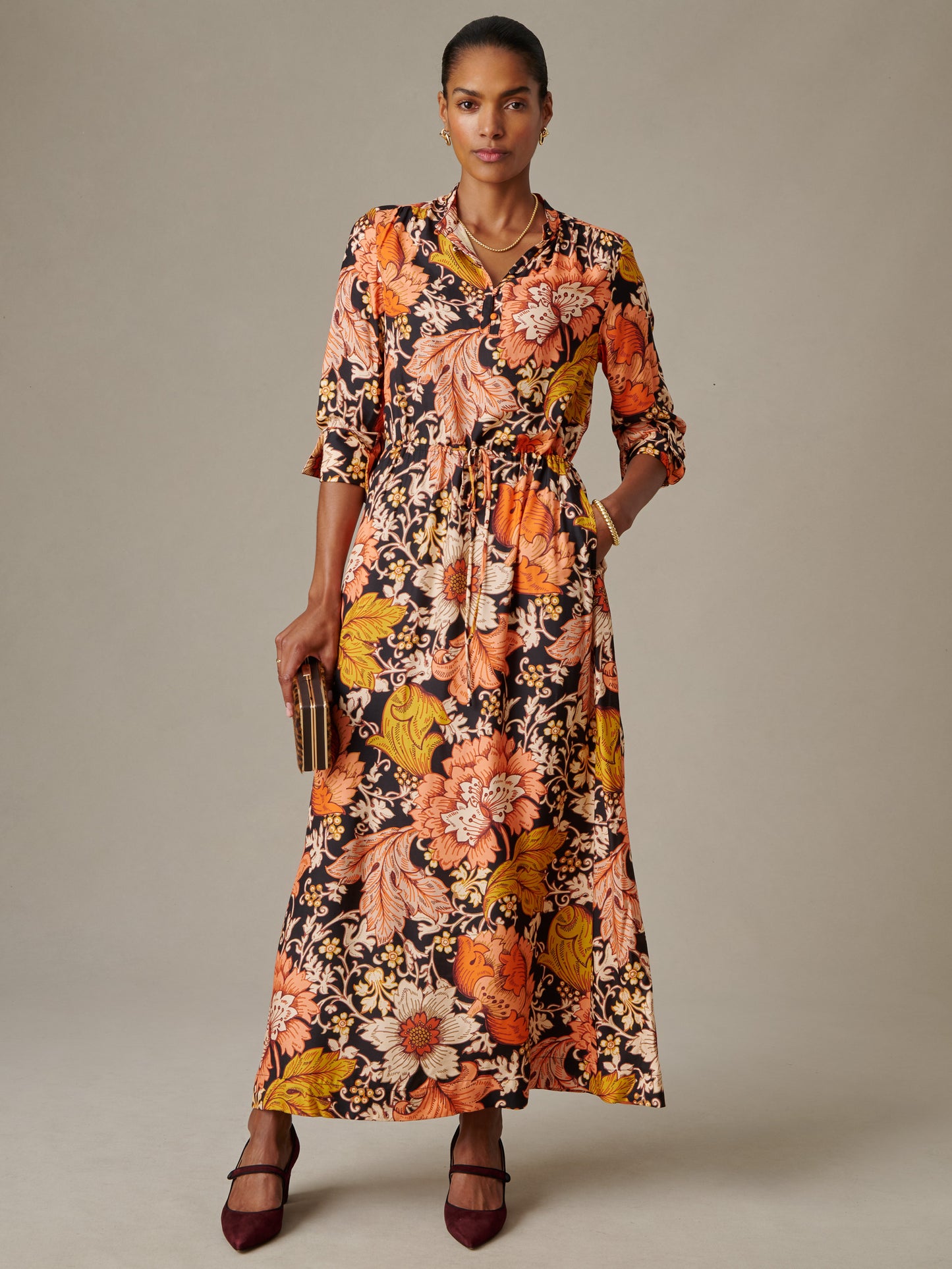 Woman wearing a Hannah Silk Blend Dress in City Garden by J.McLaughlin, featuring a vibrant floral pattern with orange, yellow, and cream tones, styled with elegant accessories and heels.