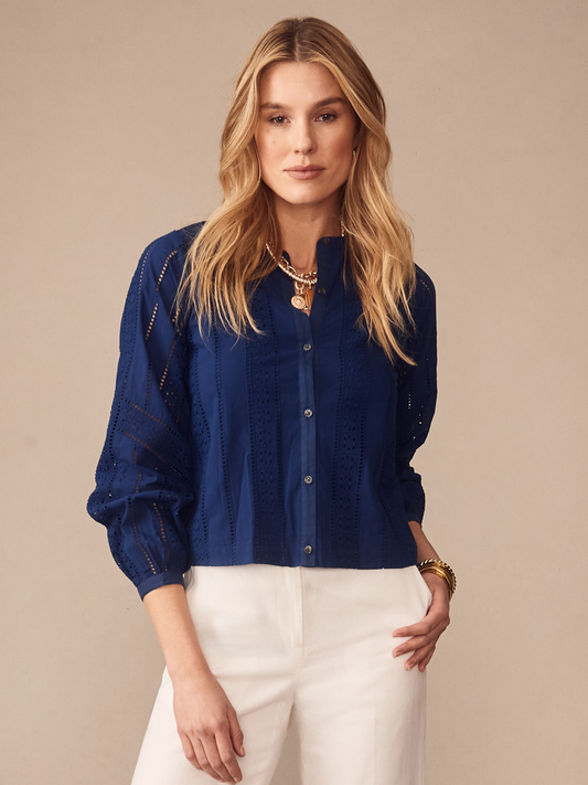 Woman wearing a nautical navy Hazel Blouse in Eyelet by J.McLaughlin, featuring intricate eyelet details and buttons, paired with white pants, showcasing effortlessly stylish, enduring designs.
