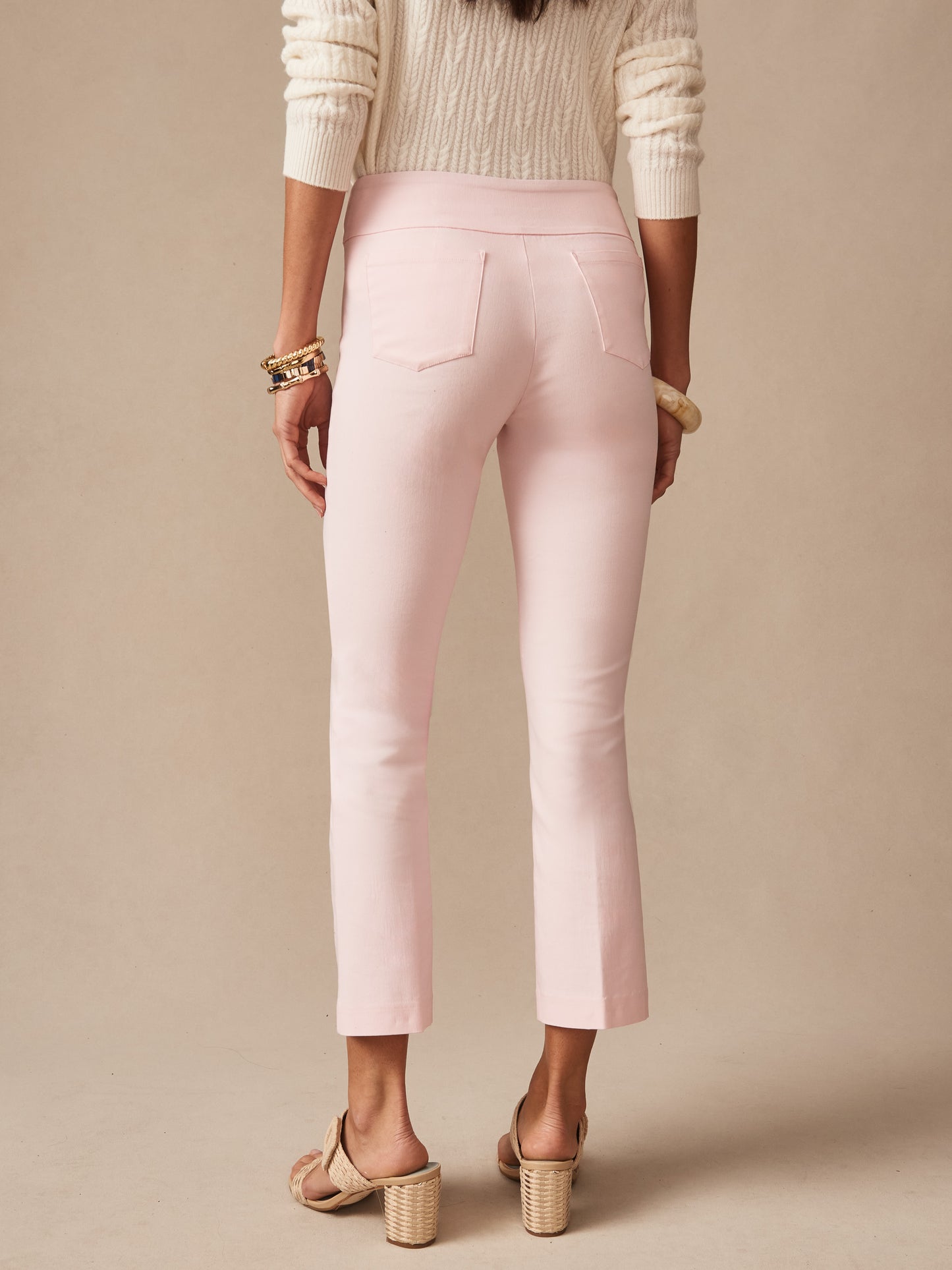 Back view of a woman wearing pale pink Ivy Pants by J.McLaughlin paired with a cream sweater and heeled sandals, showcasing effortlessly stylish, enduring designs and innovative fabrics.
