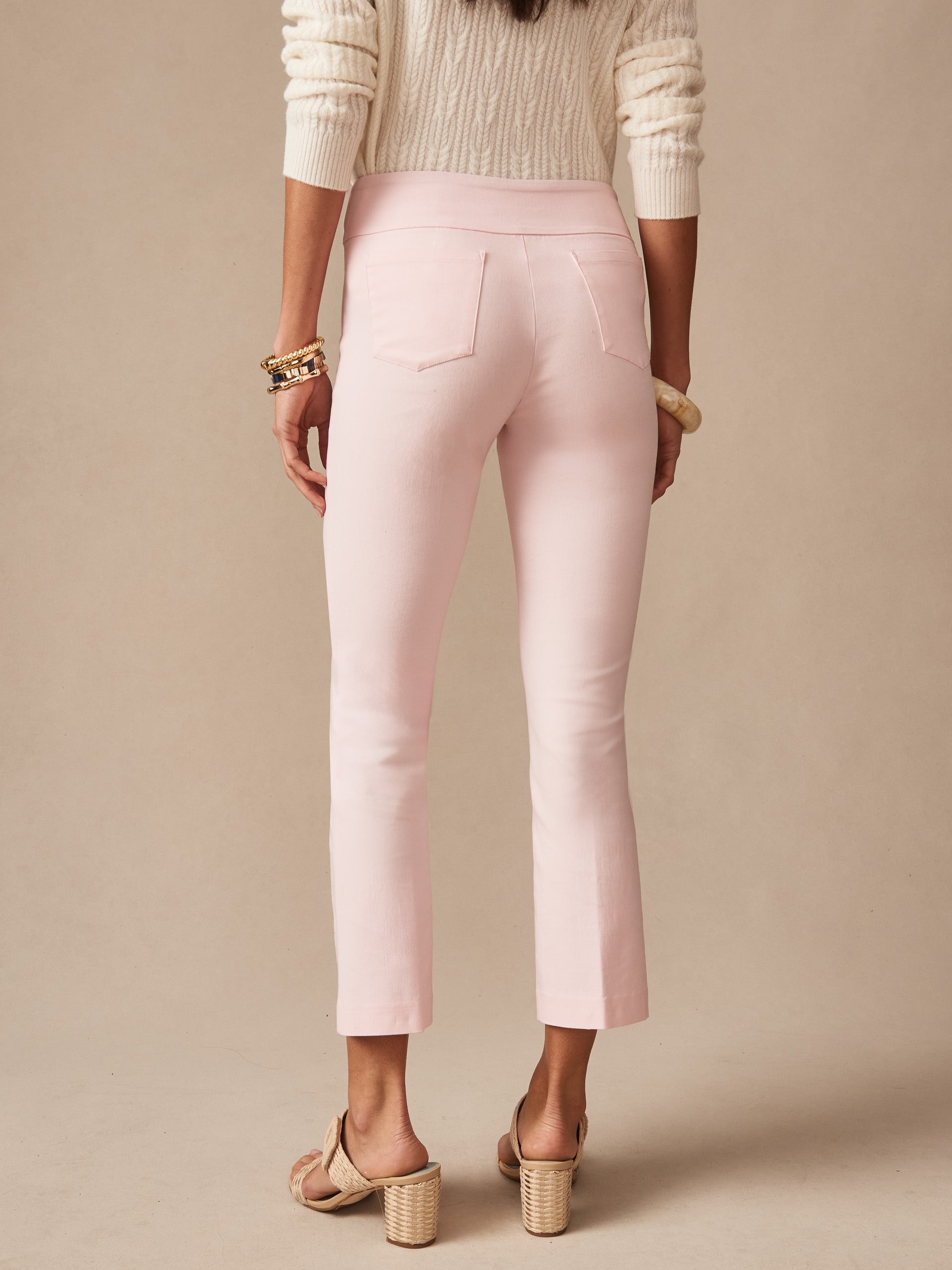 Back view of a woman wearing pale pink Ivy Pants by J.McLaughlin paired with a cream sweater and heeled sandals, showcasing effortlessly stylish, enduring designs and innovative fabrics.