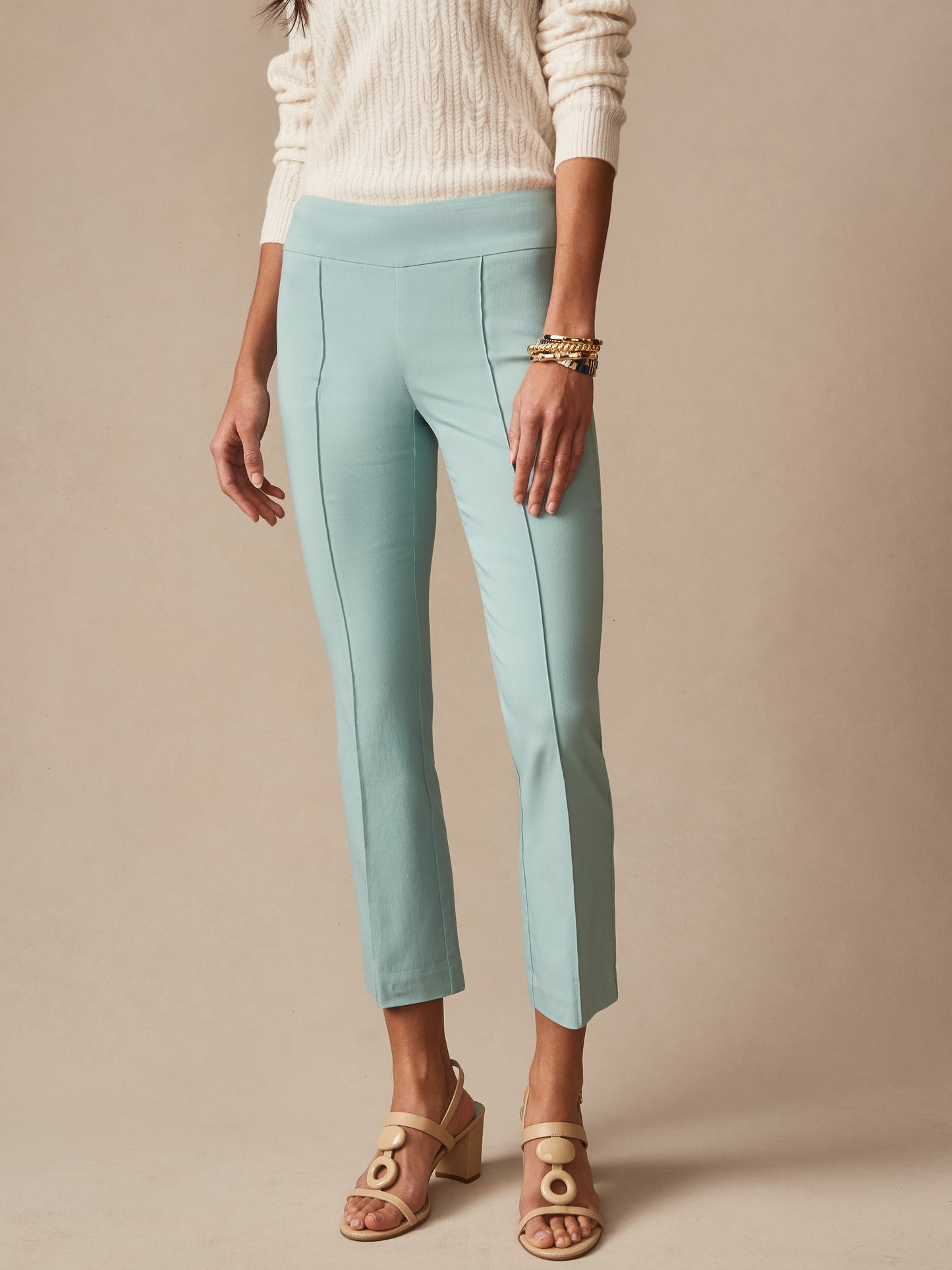 Woman wearing seafoam green Ivy Pants by J.McLaughlin paired with a cream cable-knit sweater and beige heeled sandals, showcasing effortlessly stylish and enduring designs.