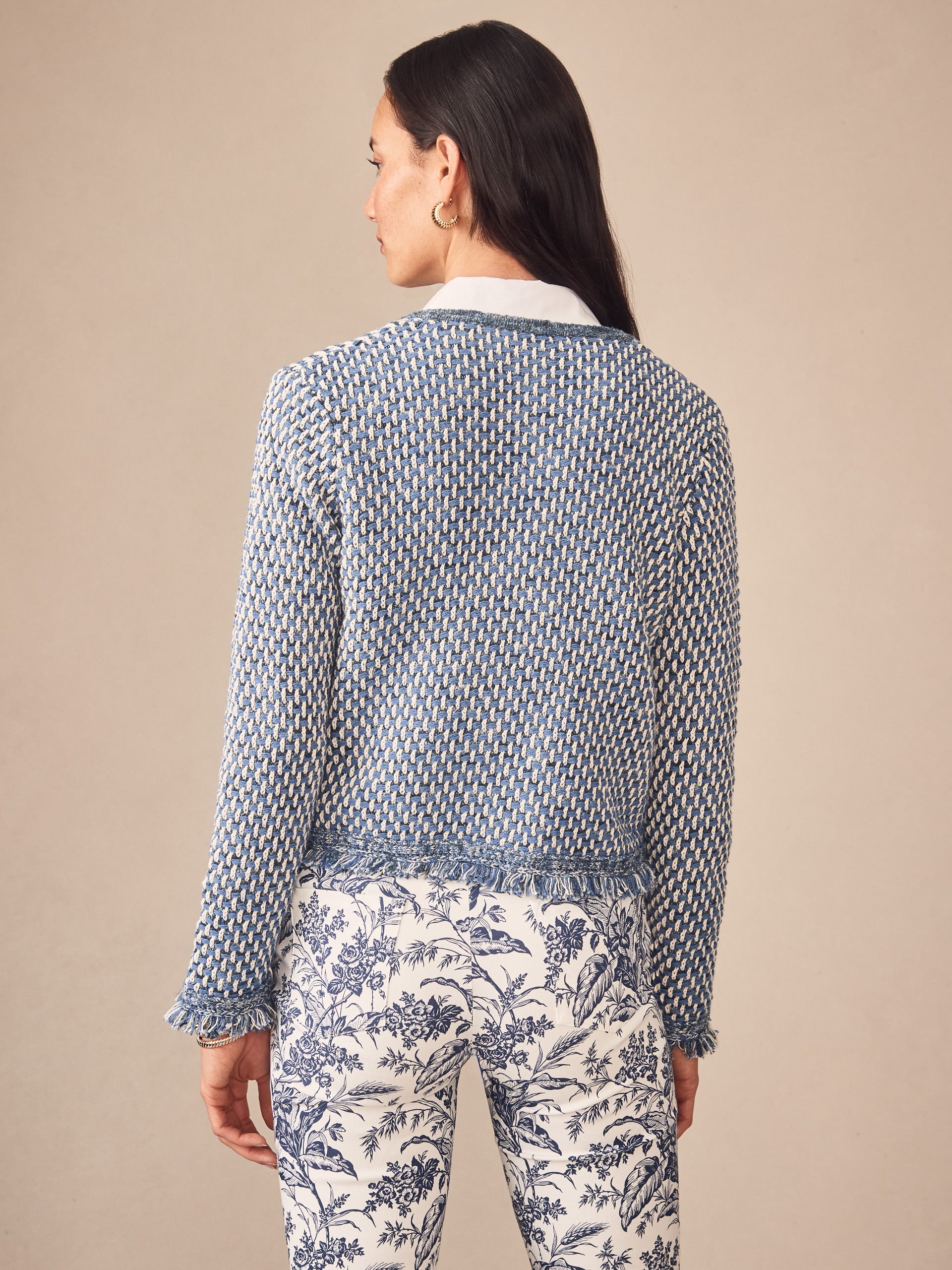 Woman wearing a blue and white textured Marceline Cardigan by J.McLaughlin paired with white pants featuring a blue floral print, showcasing effortlessly stylish, enduring designs.