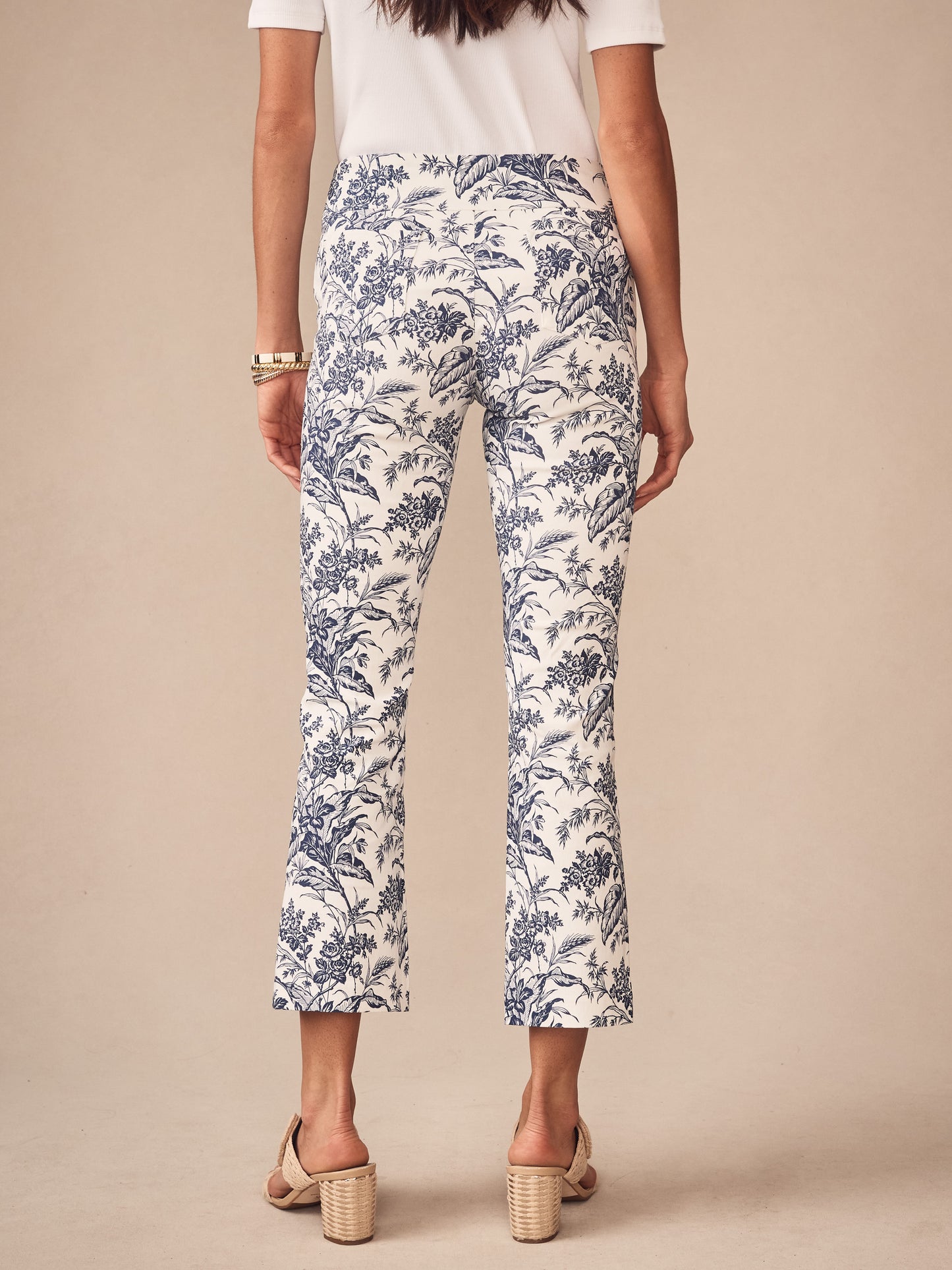 Rear view of a woman wearing J.McLaughlin Ivy Pants in Giardino Toile featuring a blue floral pattern on white fabric, paired with a white top and stylish beige block-heeled sandals, showcasing effortlessly stylish, enduring designs from a destination for defining style. Life, Well-Lived.