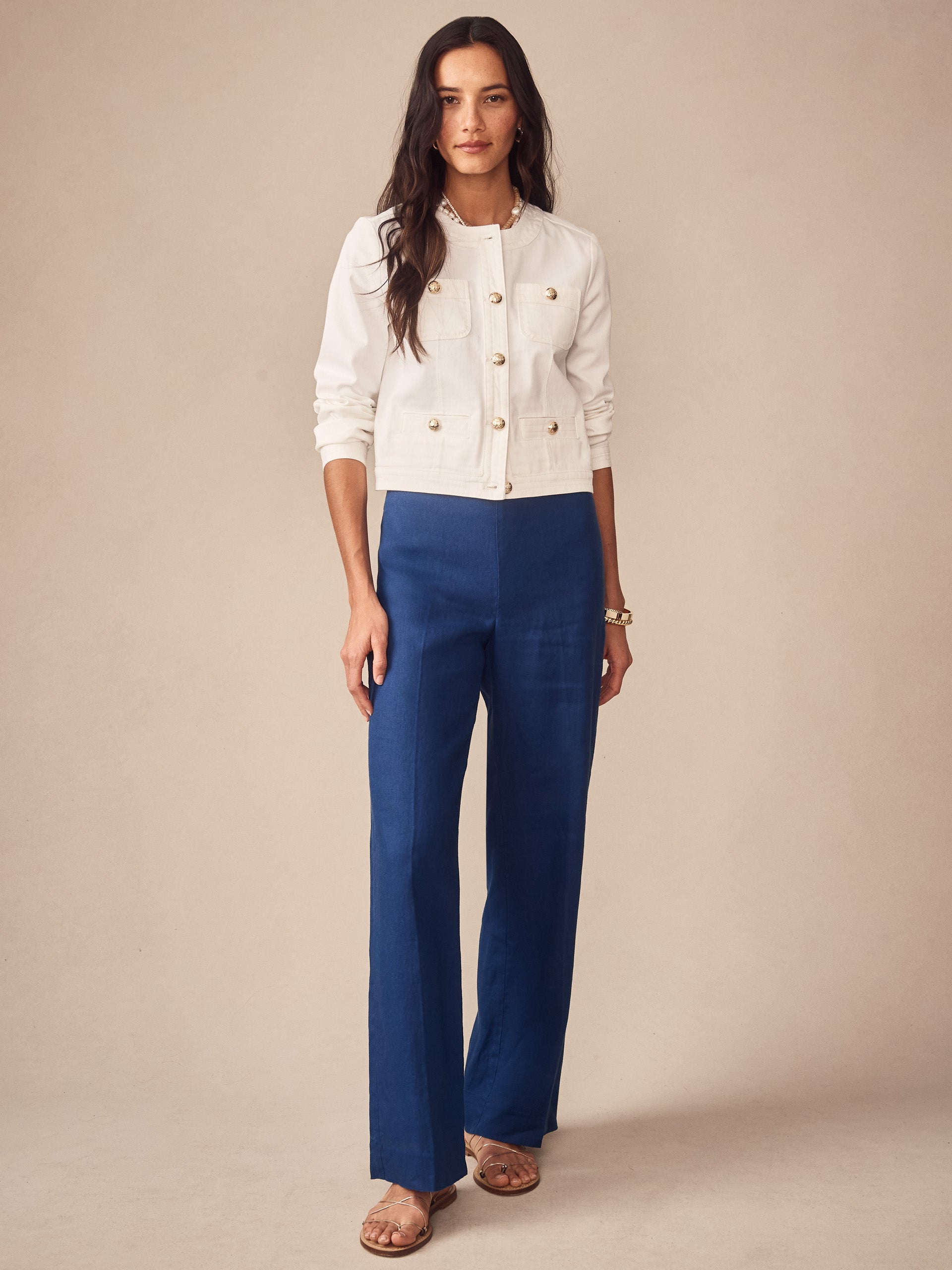 A woman wears a white Jackie Denim Jacket by J.McLaughlin paired with blue wide-leg pants, showcasing effortlessly stylish, enduring designs crafted with innovative fabrics.