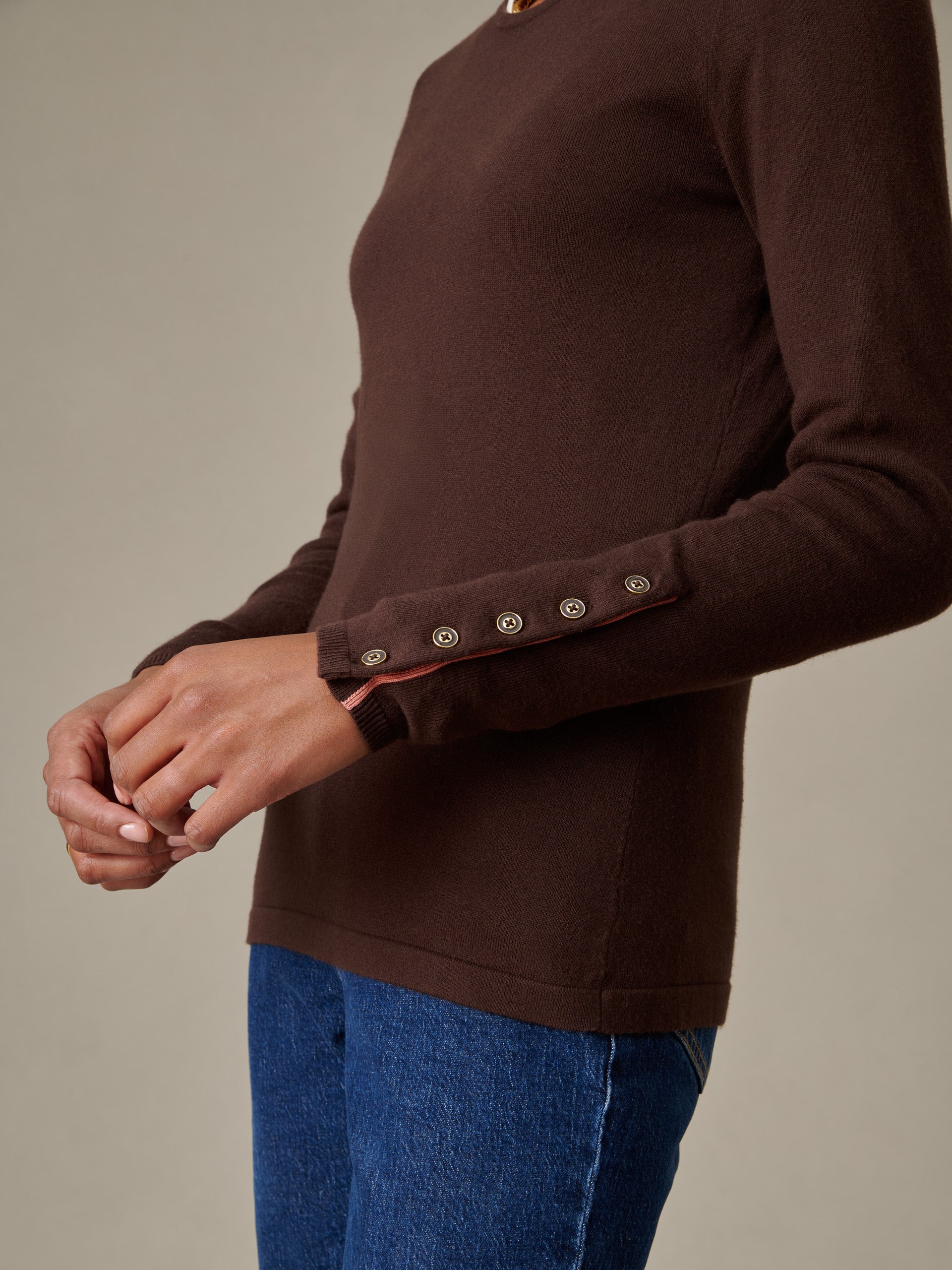 Close-up of a person wearing a brown Jamey Sweater by J.McLaughlin, featuring button details on the sleeve and paired with blue denim jeans, showcasing timeless, enduring style.