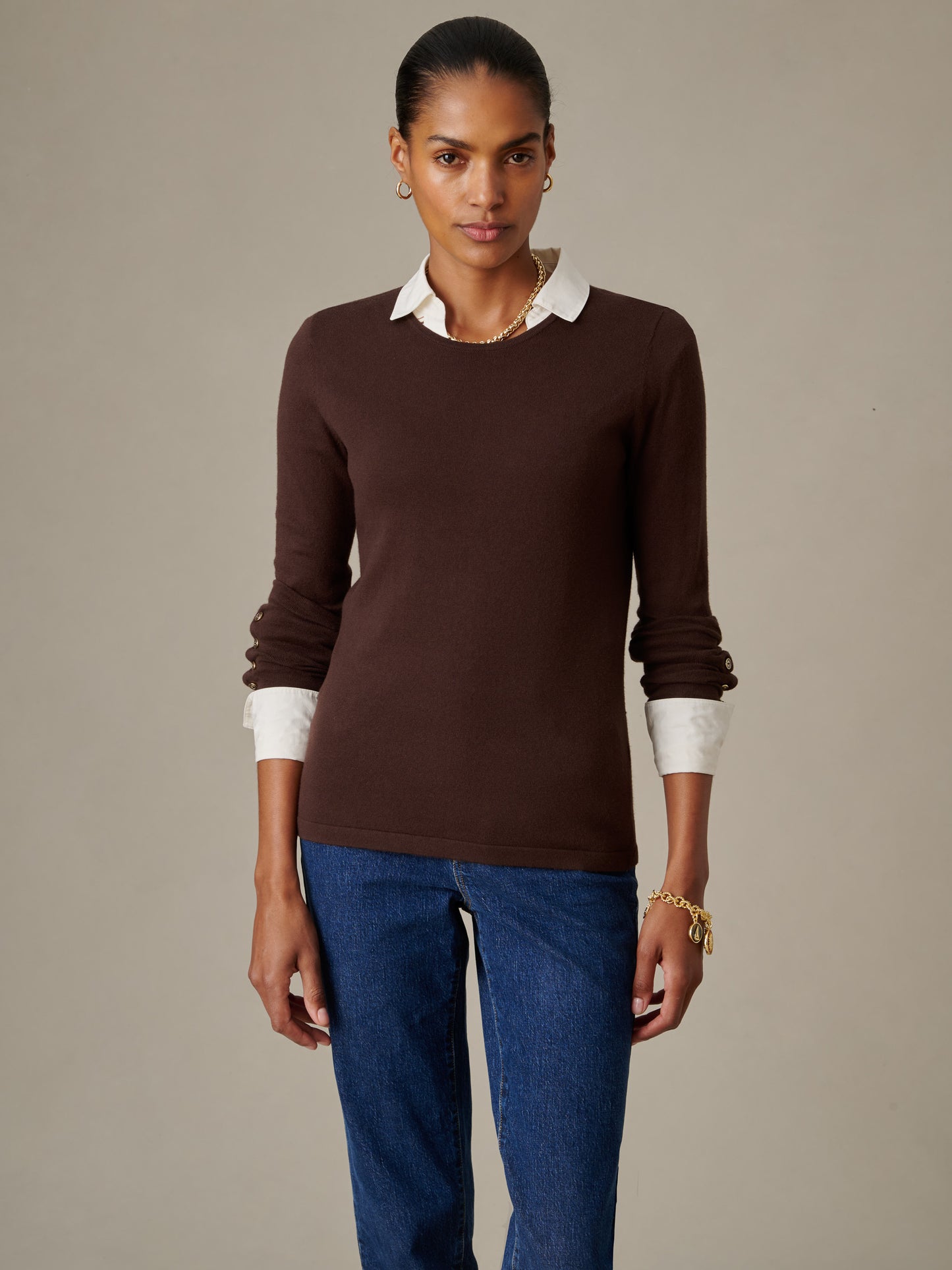 Woman wearing a fitted brown Jamey Sweater over a white collared shirt, paired with blue jeans, styled with gold hoop earrings and a bracelet, by J.McLaughlin.