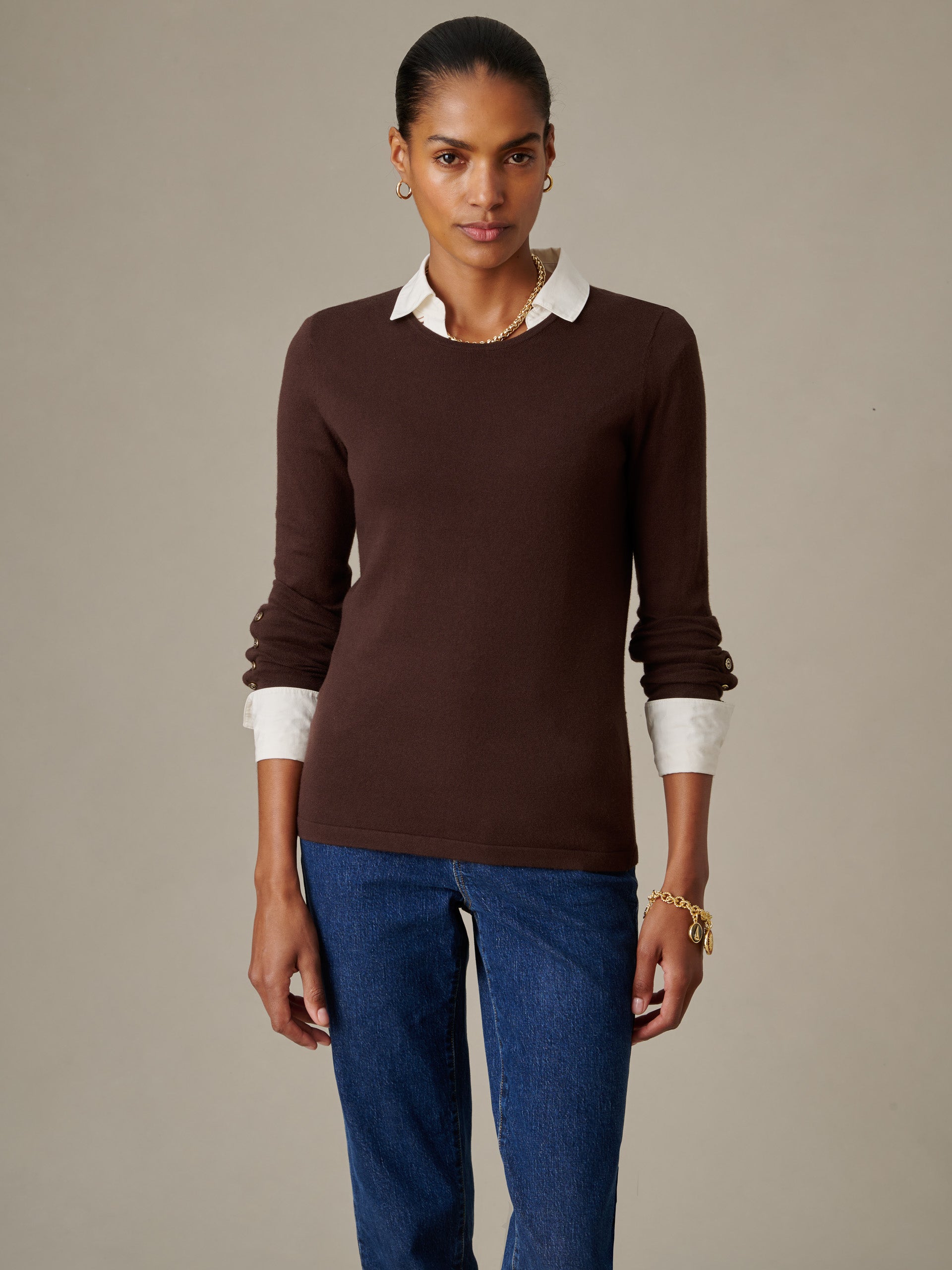 Woman wearing a fitted brown Jamey Sweater over a white collared shirt, paired with blue jeans, styled with gold hoop earrings and a bracelet, by J.McLaughlin.