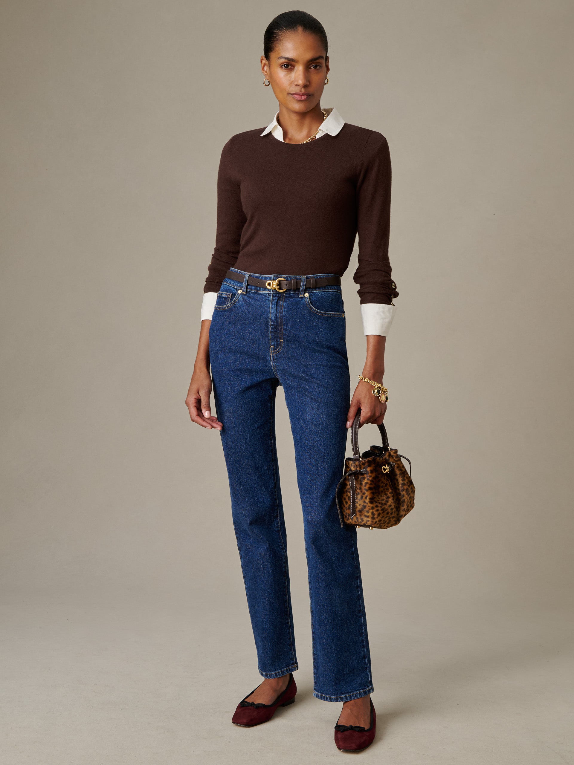 Woman wearing a J.McLaughlin Jamey Sweater in brown layered over a white collared shirt, paired with blue jeans, burgundy flats, and carrying a leopard print handbag, showcasing timeless style.