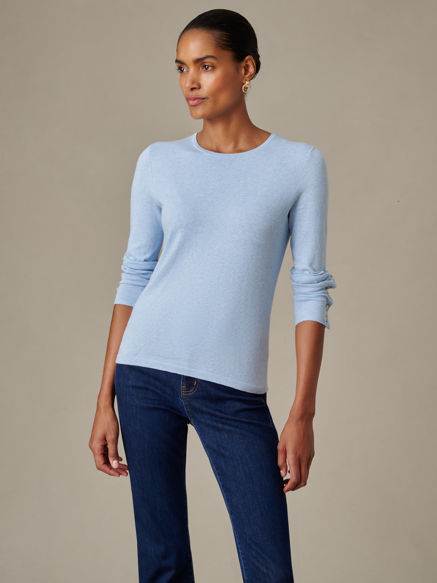 Woman wearing a light blue Jamey Sweater by J.McLaughlin paired with dark blue jeans, showcasing effortlessly stylish, enduring design and innovative fabric in a classic fit.